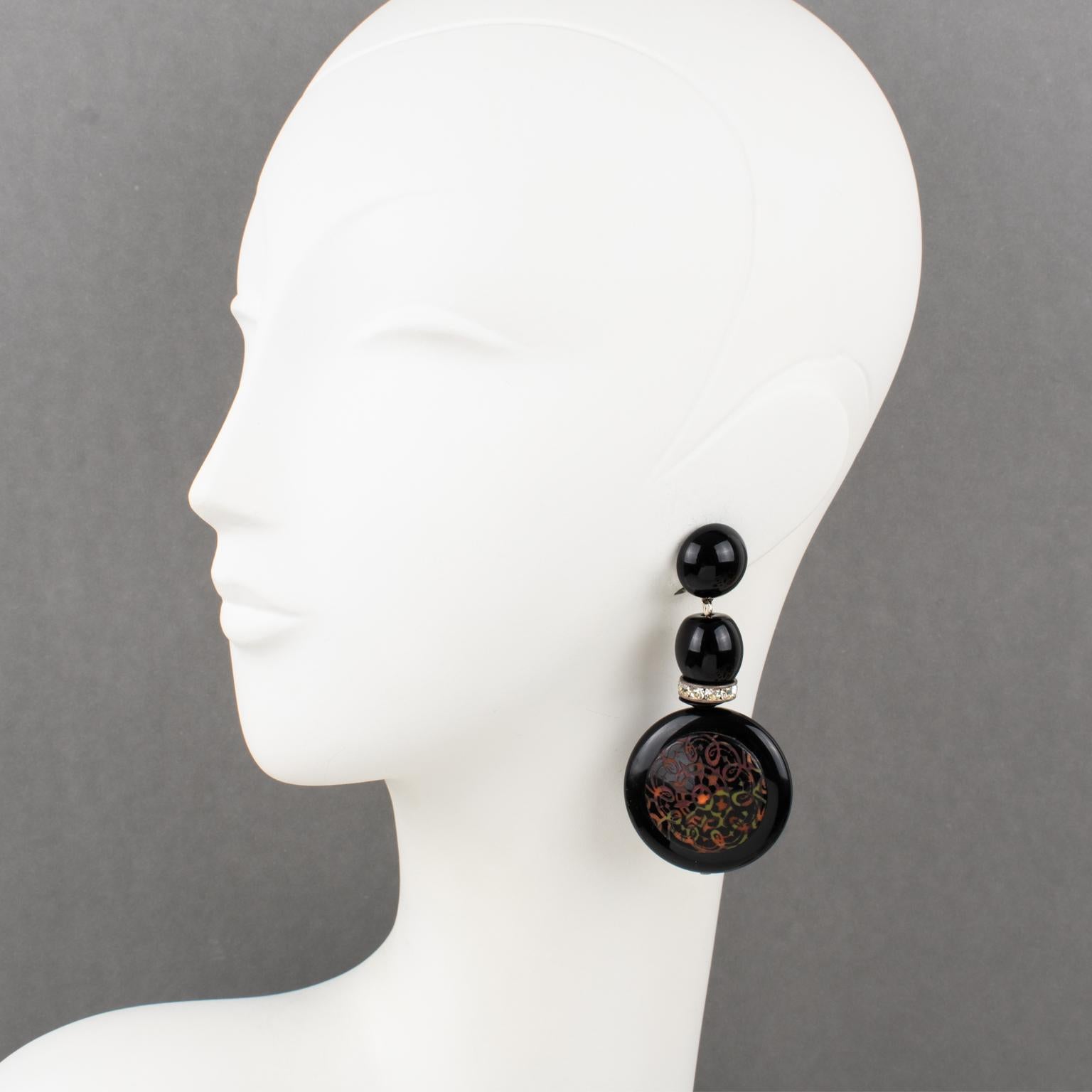 These sophisticated Angela Caputi, made-in-Italy resin clip-on earrings feature a massive dangling shape with a dimensional black color disk ornate with a multicolor floral medallion with Baroque-inspired carving. The design also boasts a black