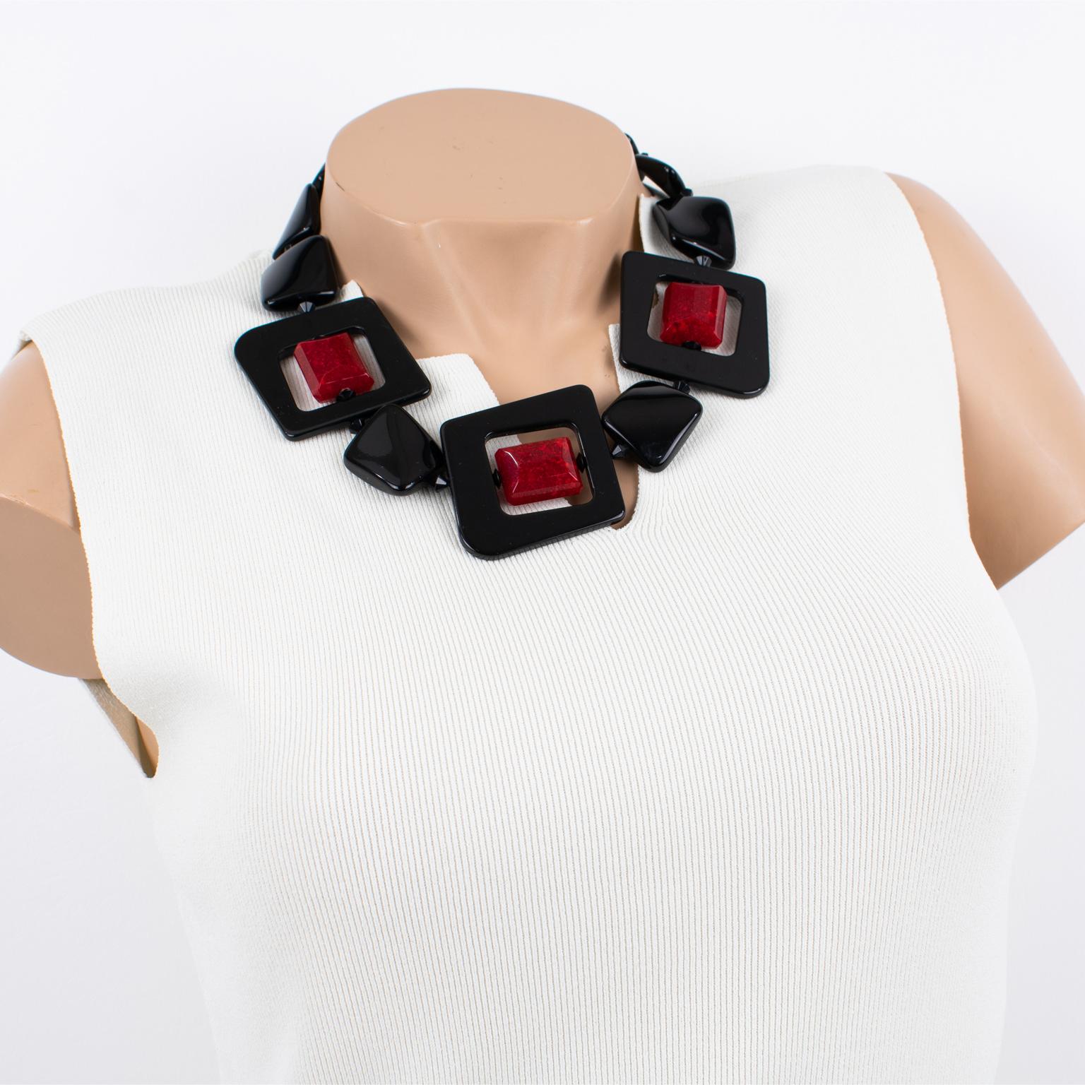 Ce joli collier en résine Angela Caputi, made in Italy, fonctionne sur le contraste noir et rouge bordeaux. Le tour de cou est composé de gros galets sculptés et de trois perles donut de forme carrée, complétés par des perles rouges rotatives. Ses