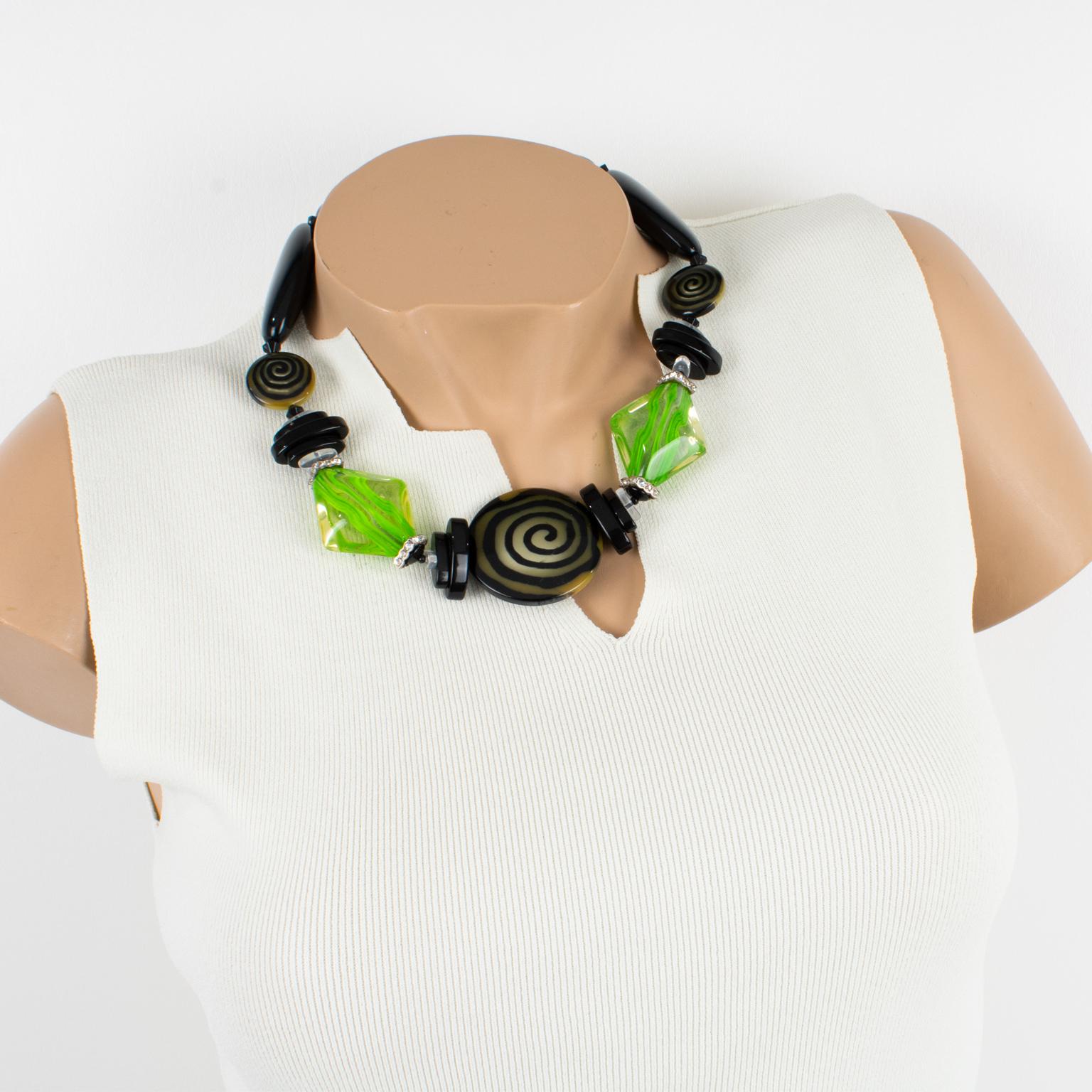 Este elegante collar gargantilla de resina Angela Caputi, fabricado en Italia, trabaja el contraste negro y verde. Presenta gruesas cuentas de guijarros tallados con una cuenta central redondeada y un dibujo de textura en espiral. Su combinación de
