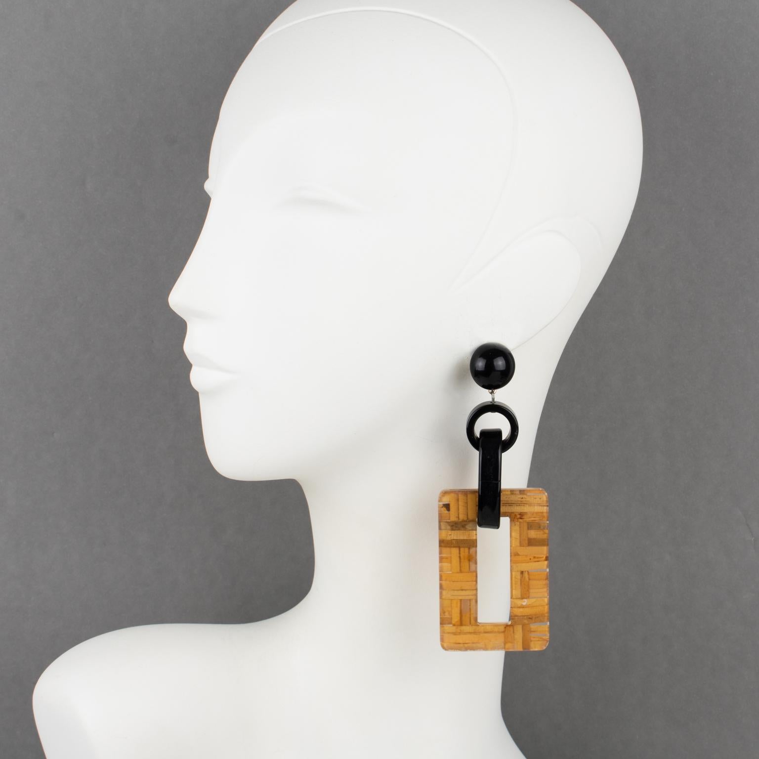 Stunning Angela Caputi made in Italy, oversized resin, and Lucite pierced earrings. A dangling shape with black resin geometric elements contrasted with a massive rectangular donut element in clear Lucite with embedded rattan or wicker. Her matching