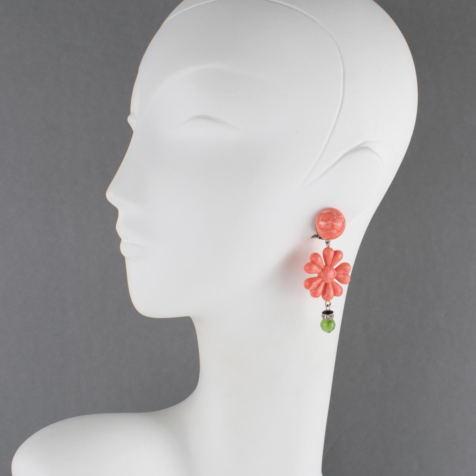 Ces étonnantes boucles d'oreilles à clip en résine Angela Caputi, fabriquées en Italie, présentent une forme pendante avec une fleur dimensionnelle stylisée en faux corail, complétée par un élément sculpté en faux-jade vert et un anneau d'espacement