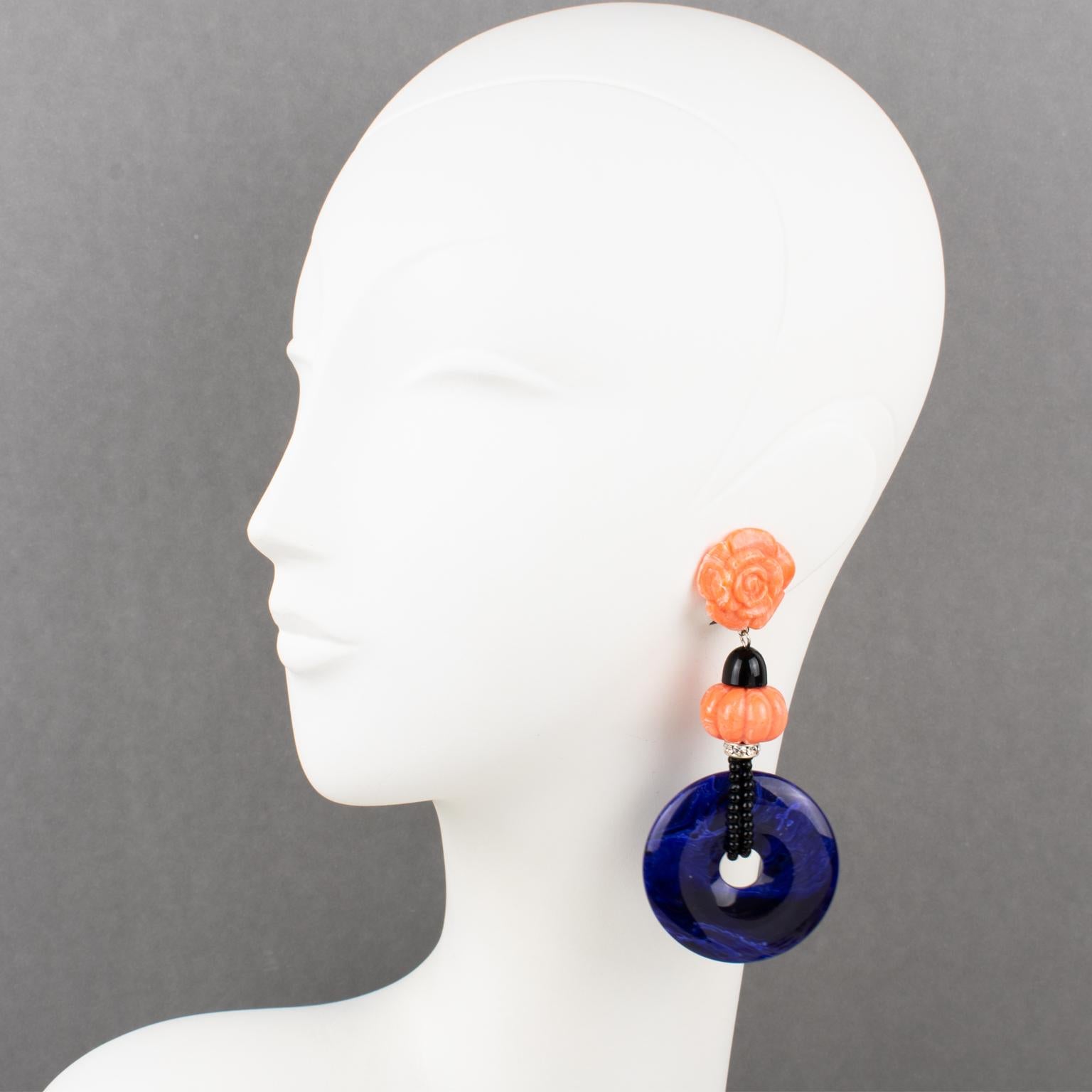 These stunning Angela Caputi, made in Italy resin clip-on earrings feature an oversized dangling shape with a dimensional stylized flower and carved bead in faux-coral color complimented with faux-Lapis blue massive donut element and tiny crystal