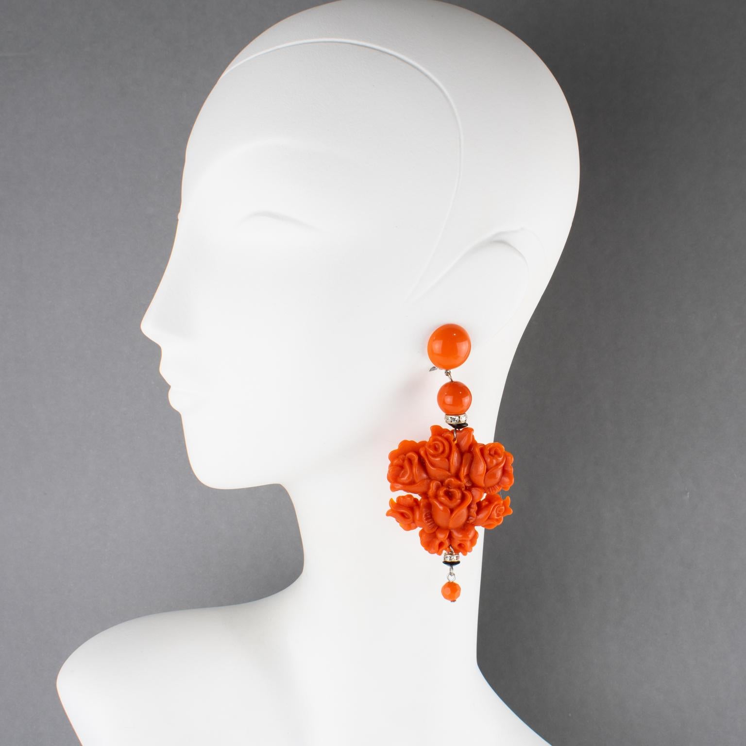 Estos impresionantes pendientes de resina con clip Angela Caputi, fabricados en Italia, presentan un diseño de gota colgante de gran tamaño con elementos florales. Los pendientes presentan grandes flores de rosa de color coral brillante,