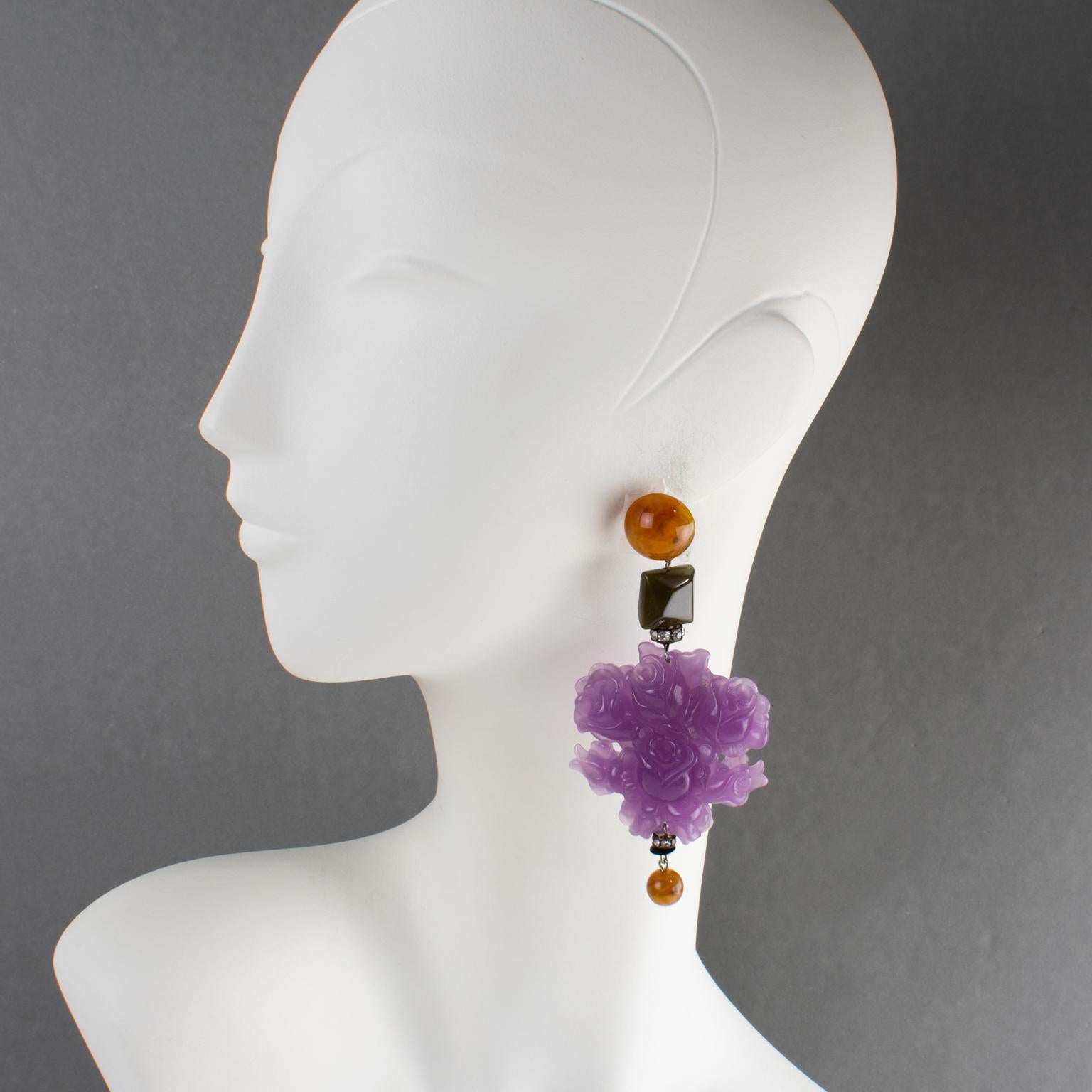 These stunning Angela Caputi resin pierced earrings, made in Italy, boast an oversized dangling-drop design with floral elements. The earrings feature large, intricately carved rose flowers in lavender purple. Dark green faceted beads, root-beer
