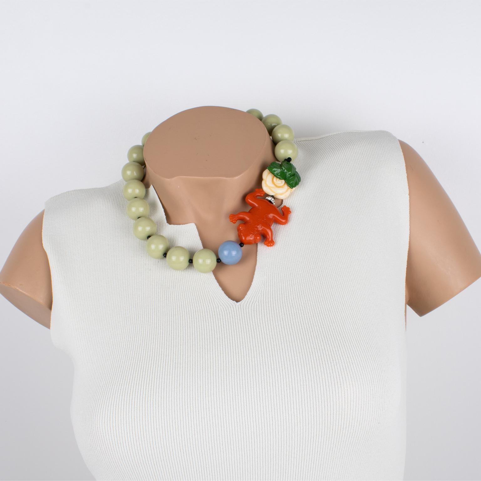 Angela Caputi designed this super cute resin choker necklace. This necklace features a set of rounded beads with a side-carved frog, flower, and leaf. It works on milky almond green and cinnabar red, contrasted with off-white, green, and baby blue.