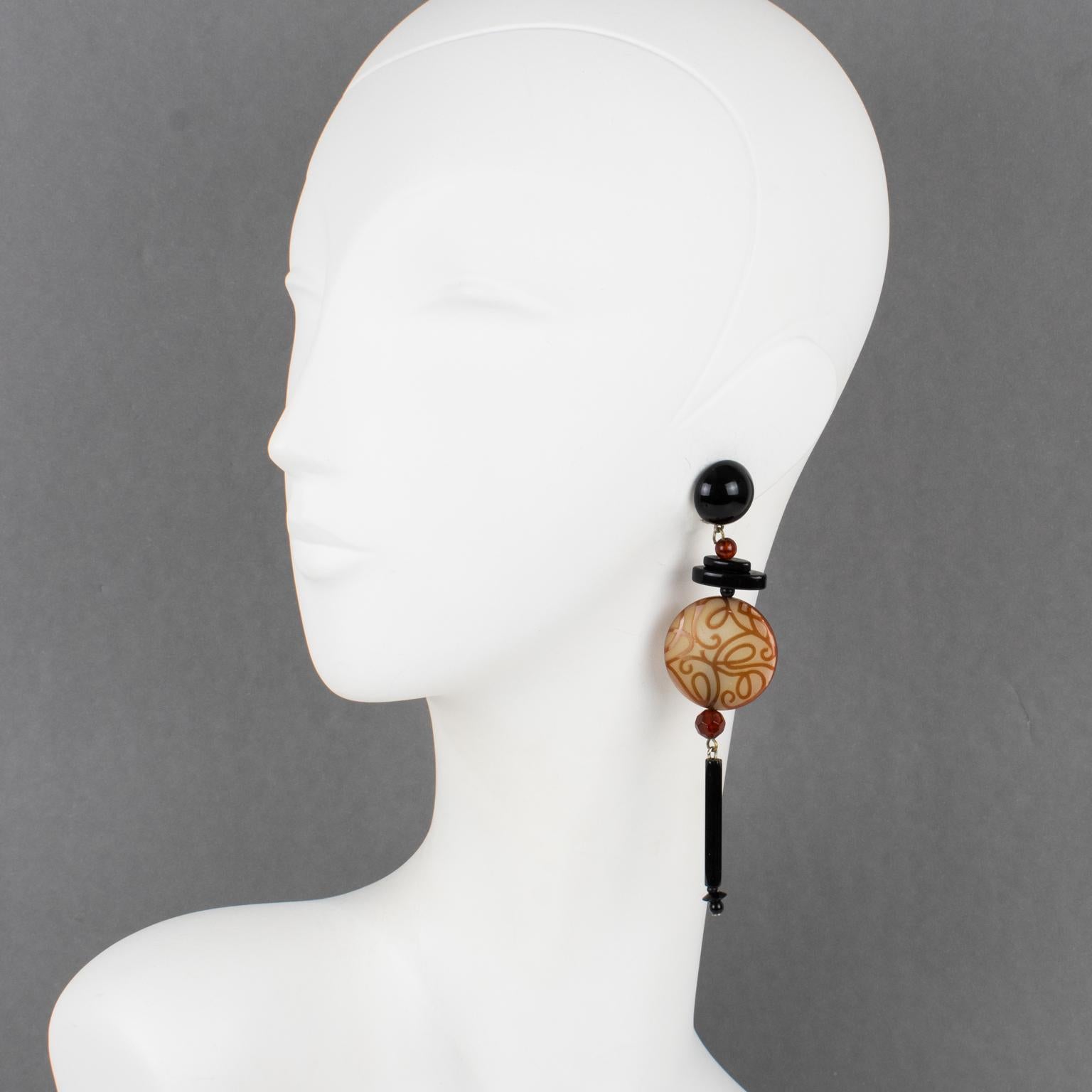 These elegant Angela Caputi resin clip-on earrings, made in Italy, feature an extra-long dangling shape with black color elements contrasted with a large milky honey flat disk ornate with an arabesque carved design. Her matching colors are always