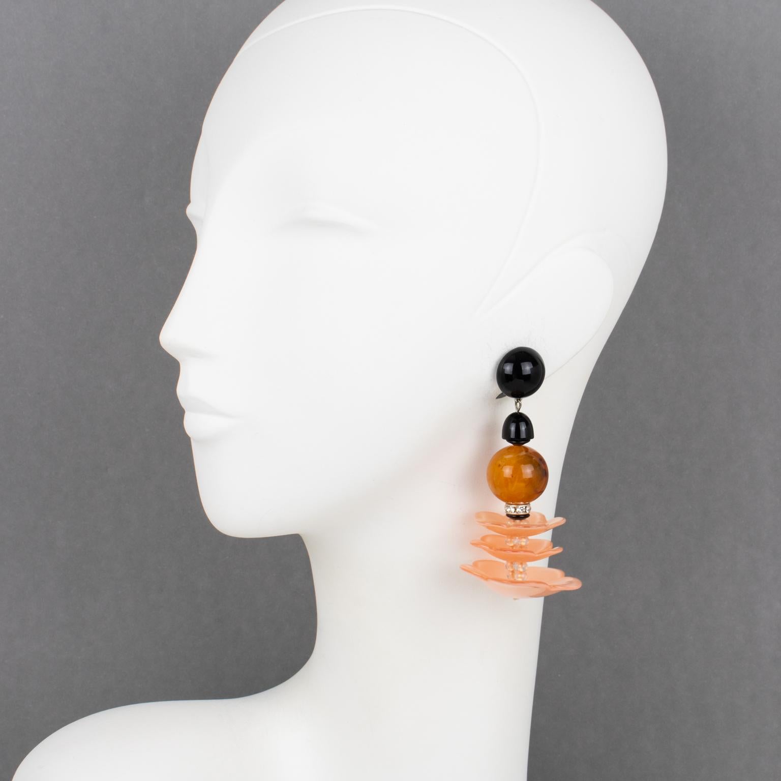 These stunning Angela Caputi, made-in-Italy resin clip-on earrings feature a massive dangling design with wavy-shaped elements. The pieces boast pink salmon, amber marble, and black colors. These earrings are from the Flamenco collection. Her color