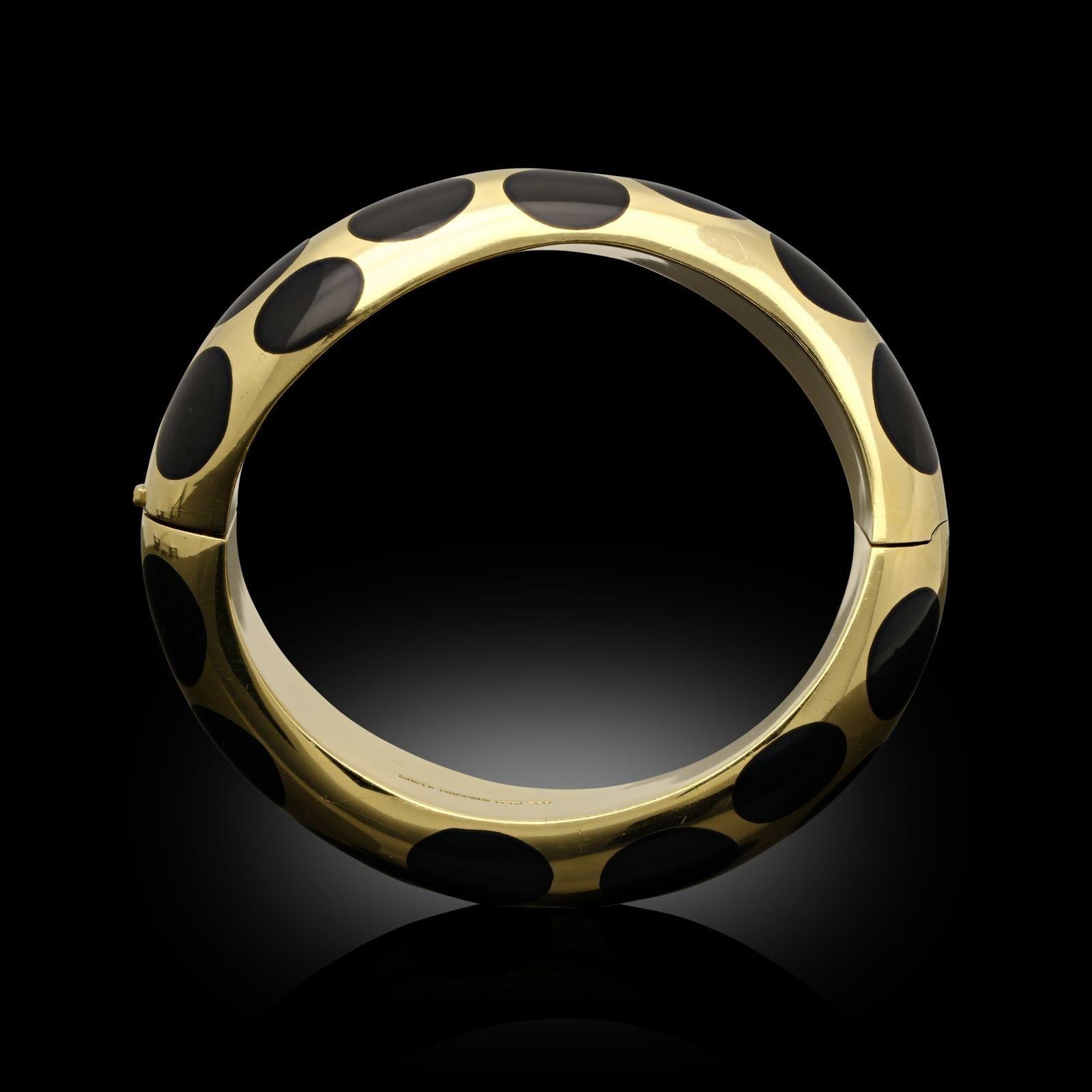A bold and striking gold and black jade bangle by Angela Cummings c.1980s, the bangle in 18ct yellow gold with rounded domed D-shape profile and curved undulating form, inlaid throughout with thirty oval carved and polished pieces of black jade, to