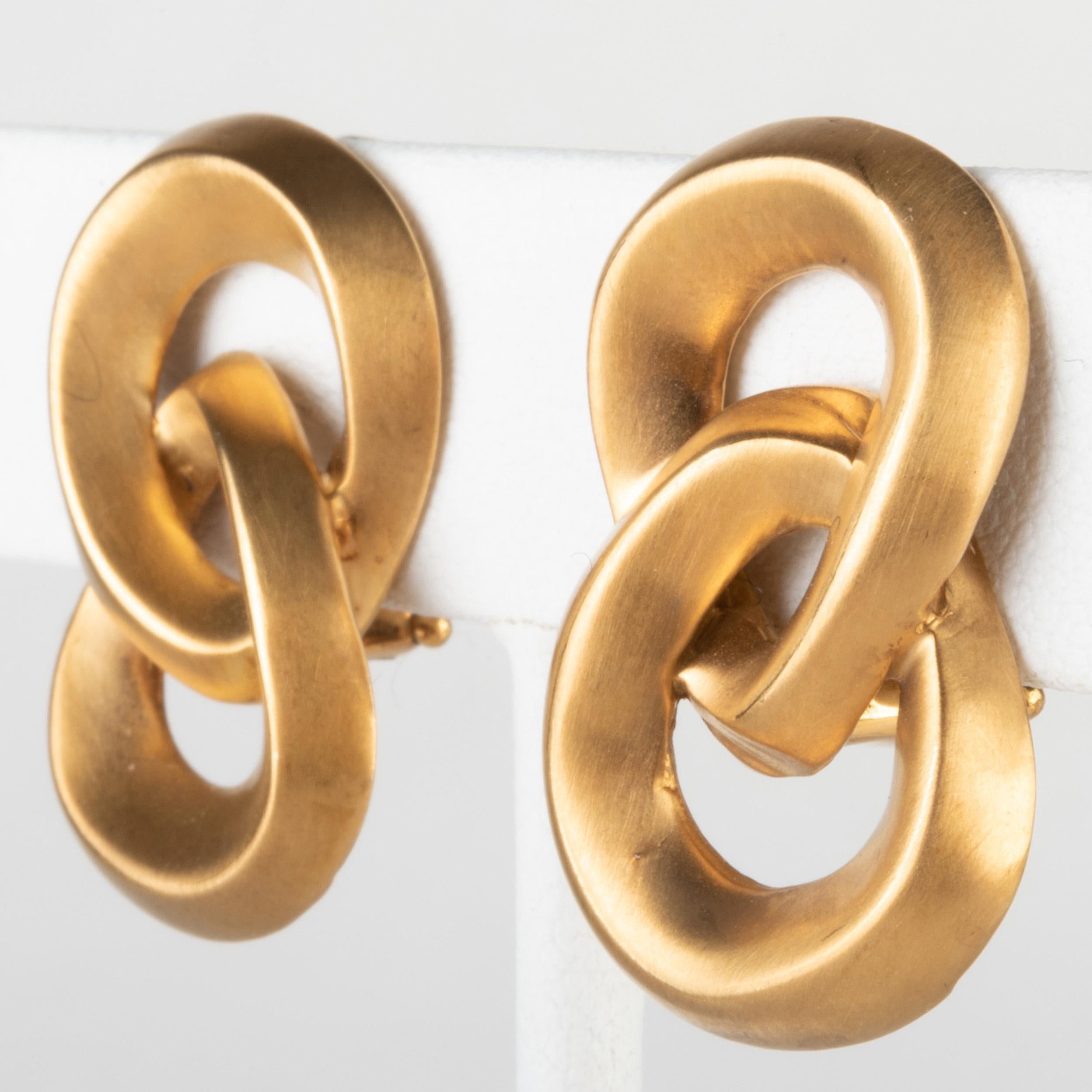 Une paire simple et élégante de boucles d'oreilles en or jaune brossé 18k par Angela Cummings.

Les boucles d'oreilles à clip sont conçues comme des nœuds entrelacés en forme de 8 avec des dos en oméga. L'or a une texture et un ton
