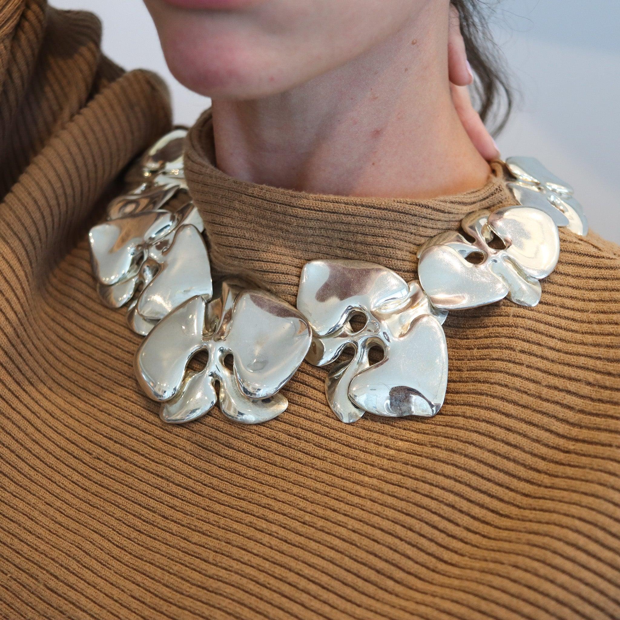 Massive Orchideen-Halskette, entworfen von Angela Cummings.

Dies ist eine überdimensionale skulpturale Halskette, die 1984 von Angela Cummings in New York City entworfen wurde. Die Halskette wurde mit organischen, freien Formen konzipiert, die