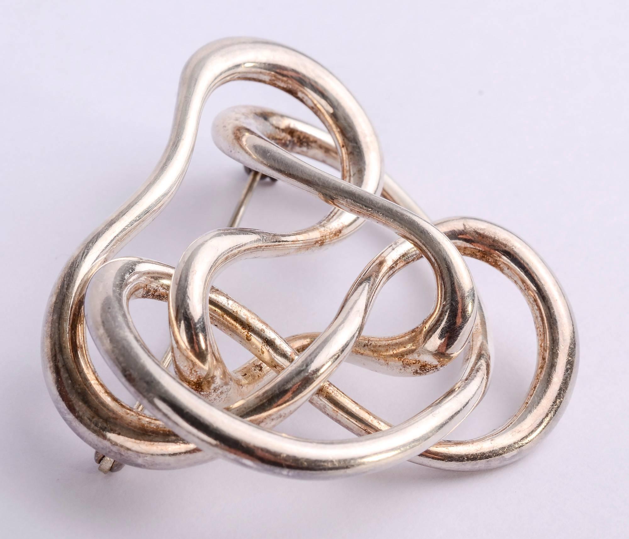 Freeform scribble brooch of sterling silver made by famed American designer, Angela Cummings. The brooch is dated 1987. It measures 2 inches wide and 1 3/4 inches tall. The silver squiggles are intertwined with space between them giving