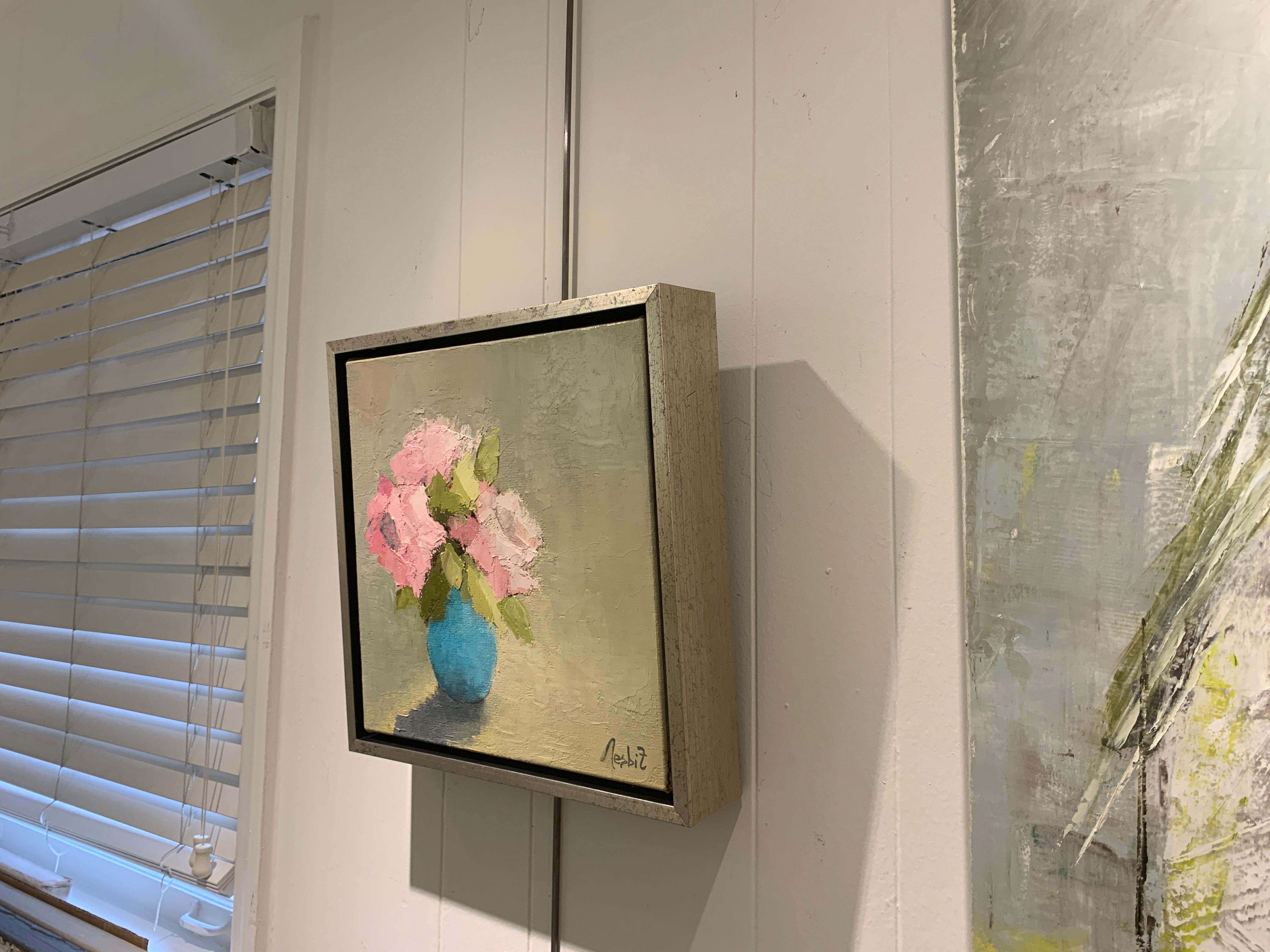 This petite impressionist 2019 painting from American artist Angela Nesbit depicts pink flowers in a glass vase.  Green, blue, grey and pink can be found in the soft and subtle palette.  The artist signed this piece on the bottom left. Unframed,