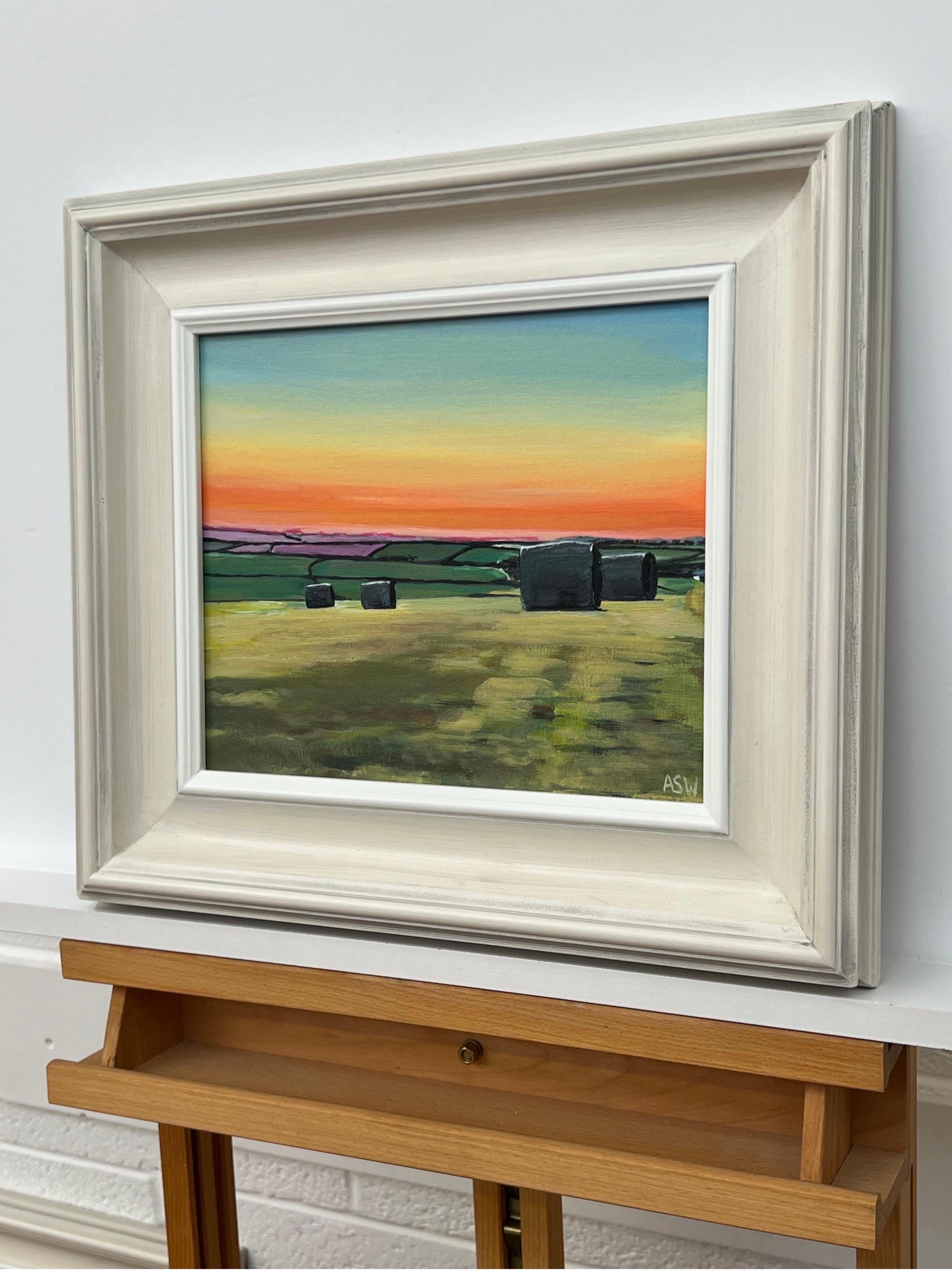 Hay Bales in Devon at Summer Sunset in the English Countryside by Contemporary British Artist, Angela Wakefield. A colourful depiction of a warm orange sunset during hay baling season at a farm on the south coast of England, with lush green fields
