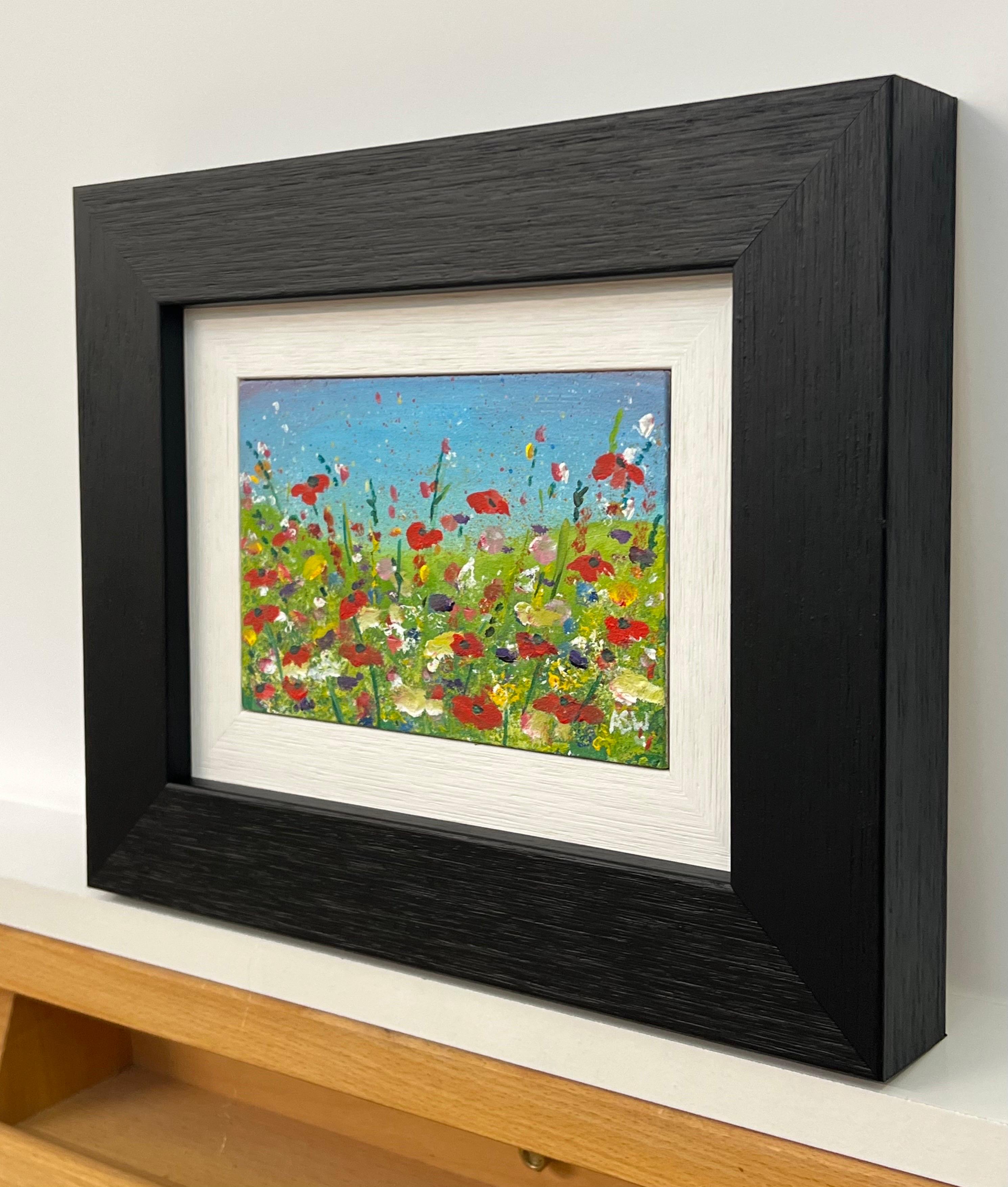 Rote Mohnblumen in Miniaturformat auf einer wilden grünen Wiese mit blauem Himmel in der englischen Landschaft von der zeitgenössischen britischen Künstlerin Angela Wakefield. Eingerahmt in einer zeitgenössischen schwarzen Leiste mit weißem Einsatz.
