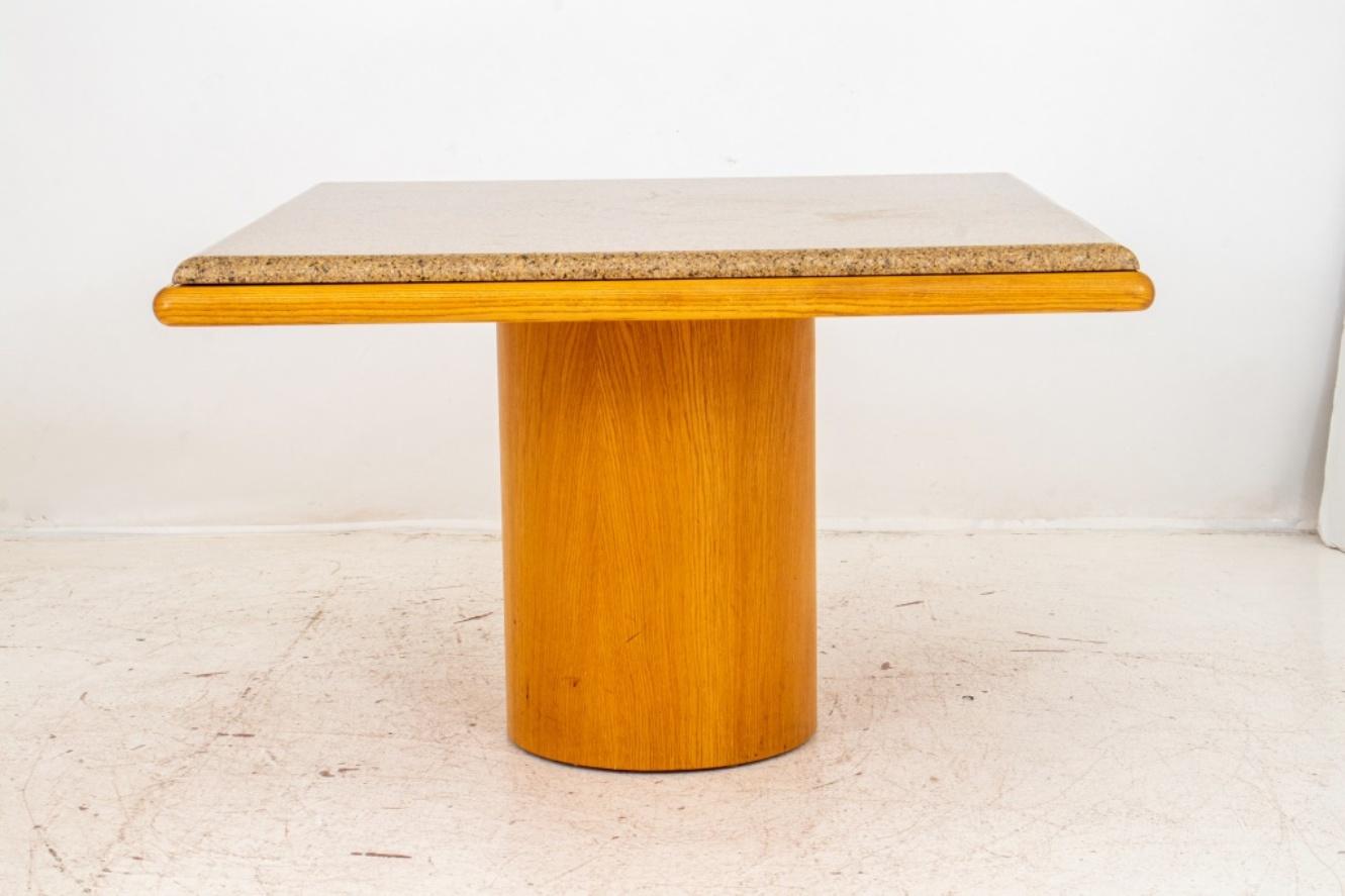 Angelo Donghia (American, 1935-1985) post modern style square granite and ash wood pedestal table, 1980s, the square gray granite top above an ash top on an ash pedestal base. 

Dealer: S138XX.