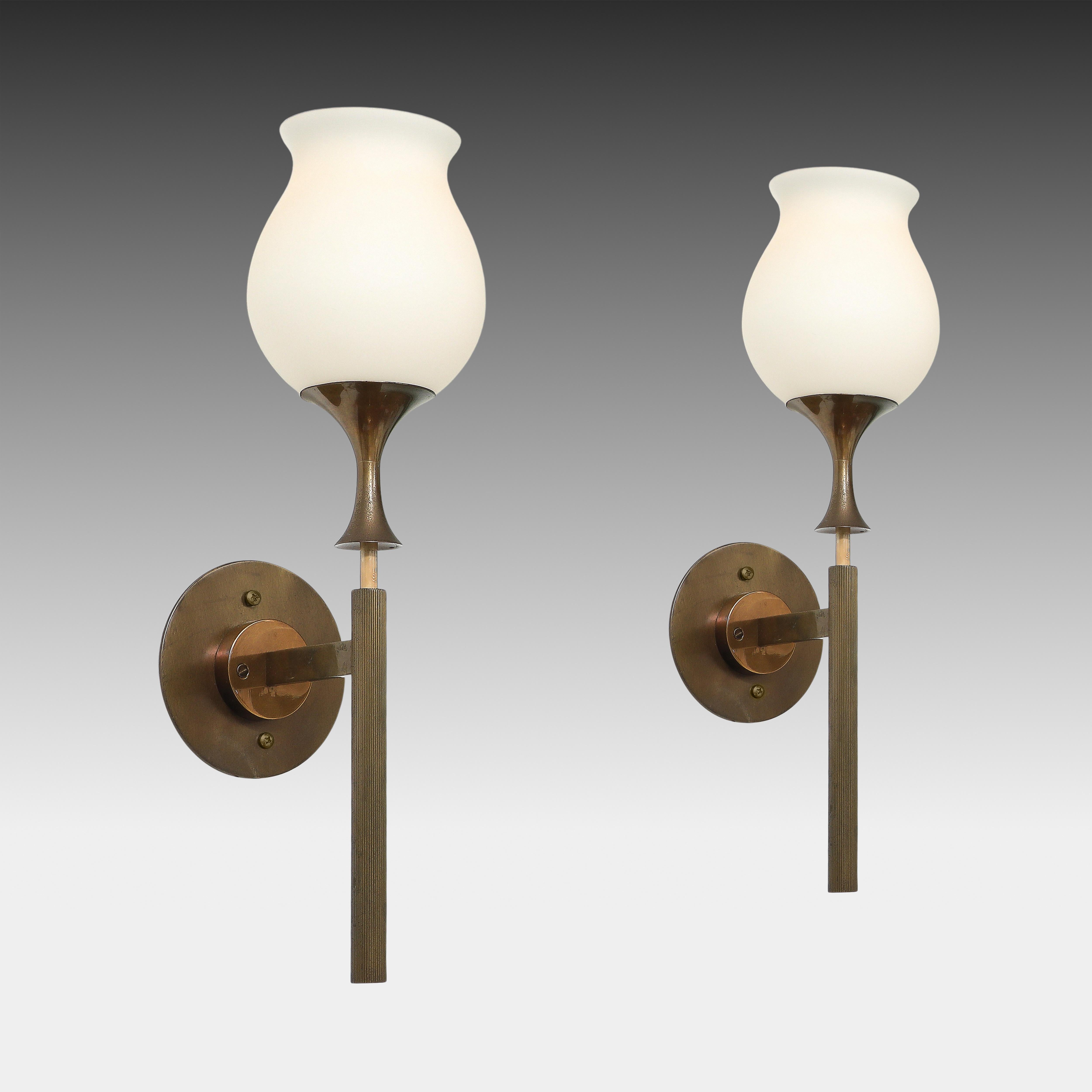 Angelo Lelii para Arredoluce Raro par de elegantes apliques largos formados por estructuras o vástagos de latón pulido lacado con difusores de cristal blanco opalino o esmerilado en forma de flor, Italia, hacia 1956. Estos preciosos apliques