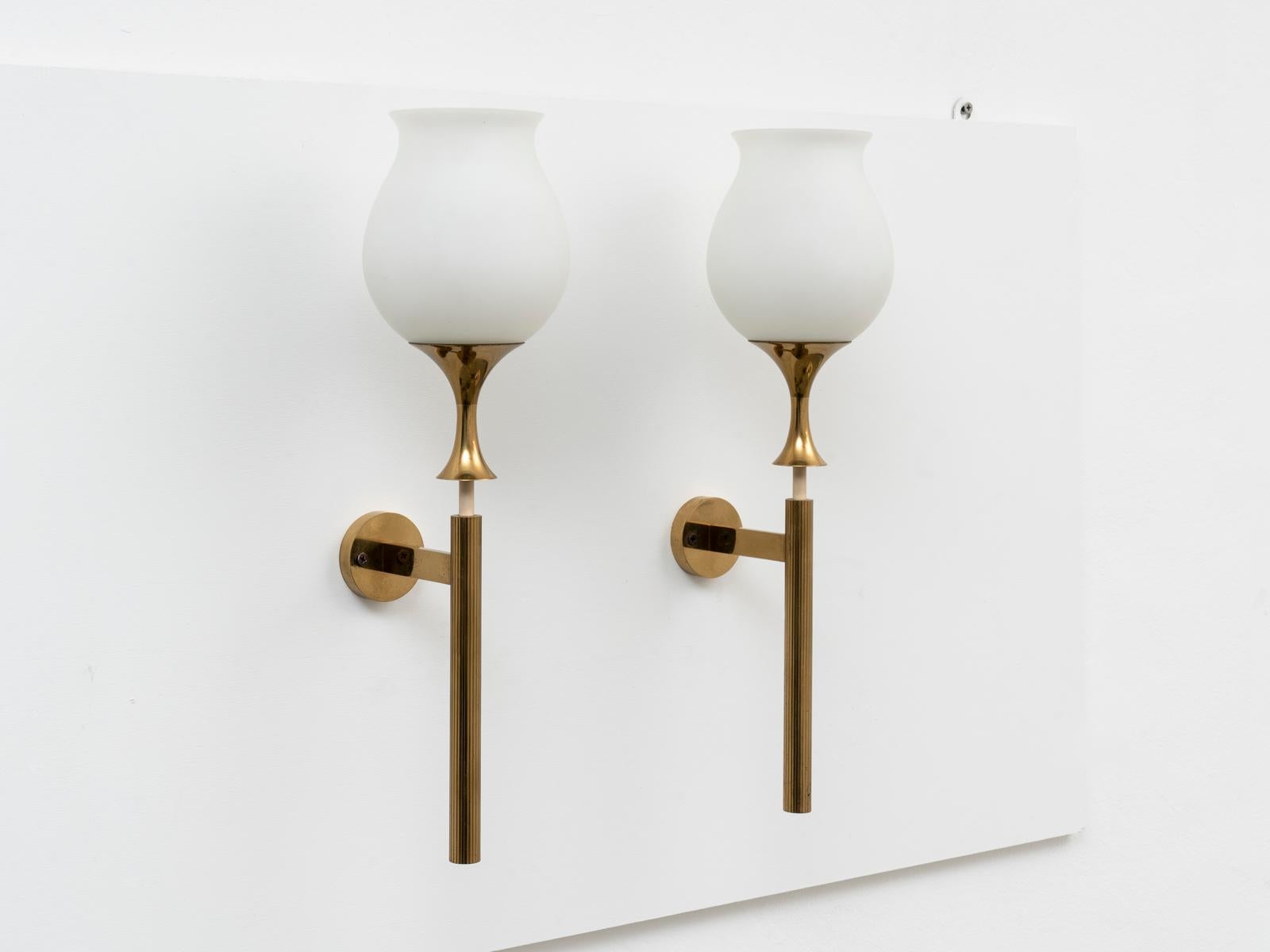 This pair of wall lights was designed by Italian lighting master Angelo Lelii (also known as Lelli) for Arredoluce in 1956. They are made of a polished brass structure with duplex-opal glass shades. They mount a E27 lightbulb each and could be
