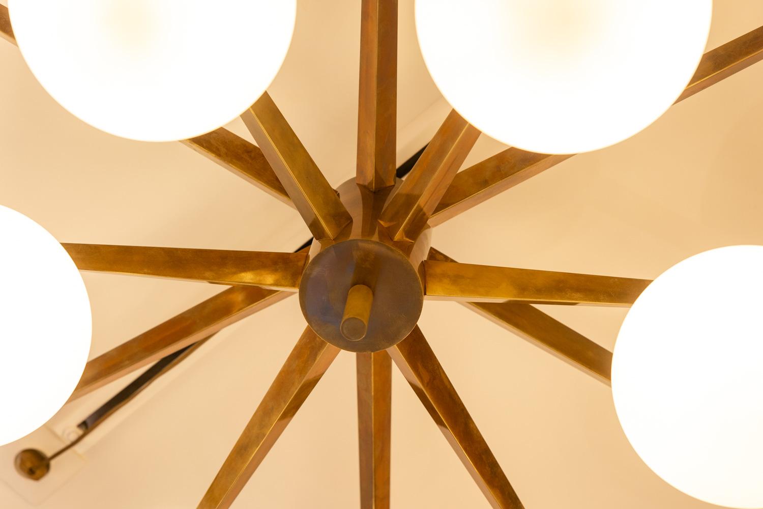 Angelo Lelli for Arredoluce, in the style of.

Chandelier. Frame in matt gilded brass with a decorative circular part in its center, with 12 finely beveled arms of light with their round-shaped white opalines.

Contemporary Italian work in small