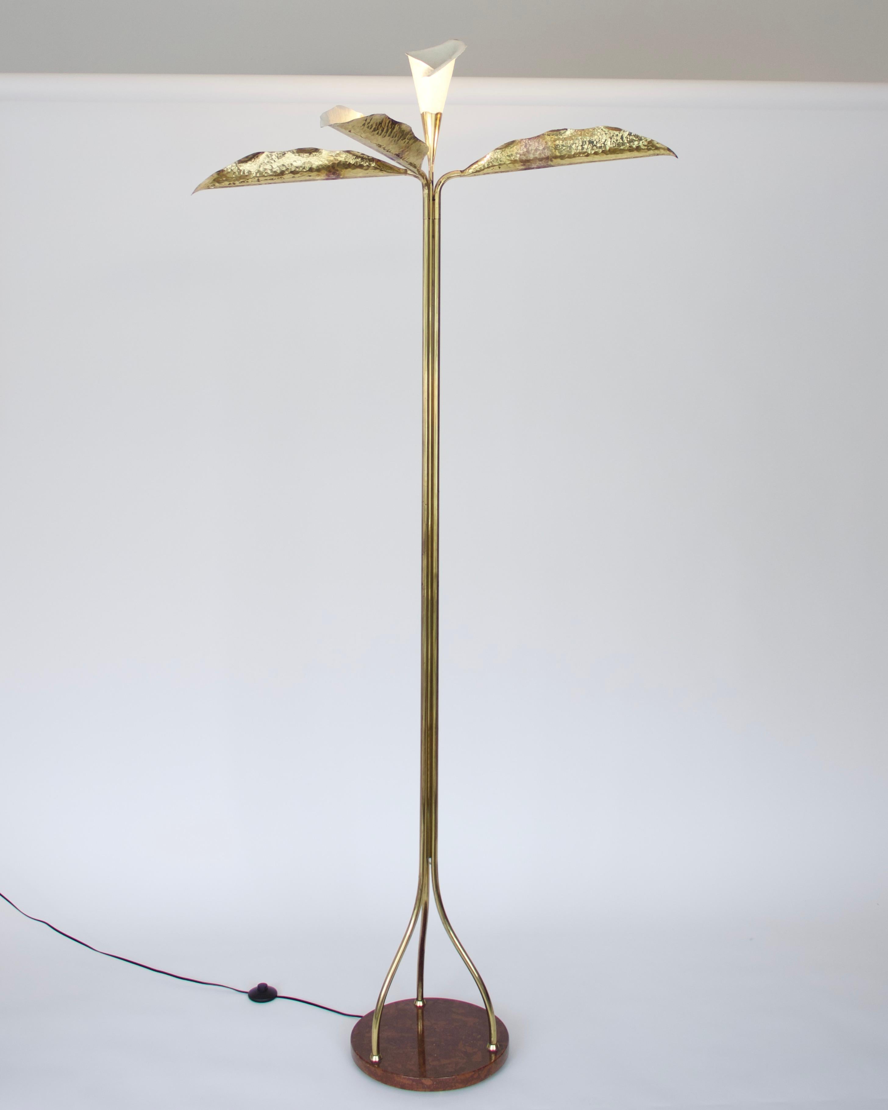 This Angelo Lelli floor lamp is comprised of three hammered brass illuminated leaf forms, surrounding an illuminated calla lily that terminates at the bottom in a tri-leg base within a 1