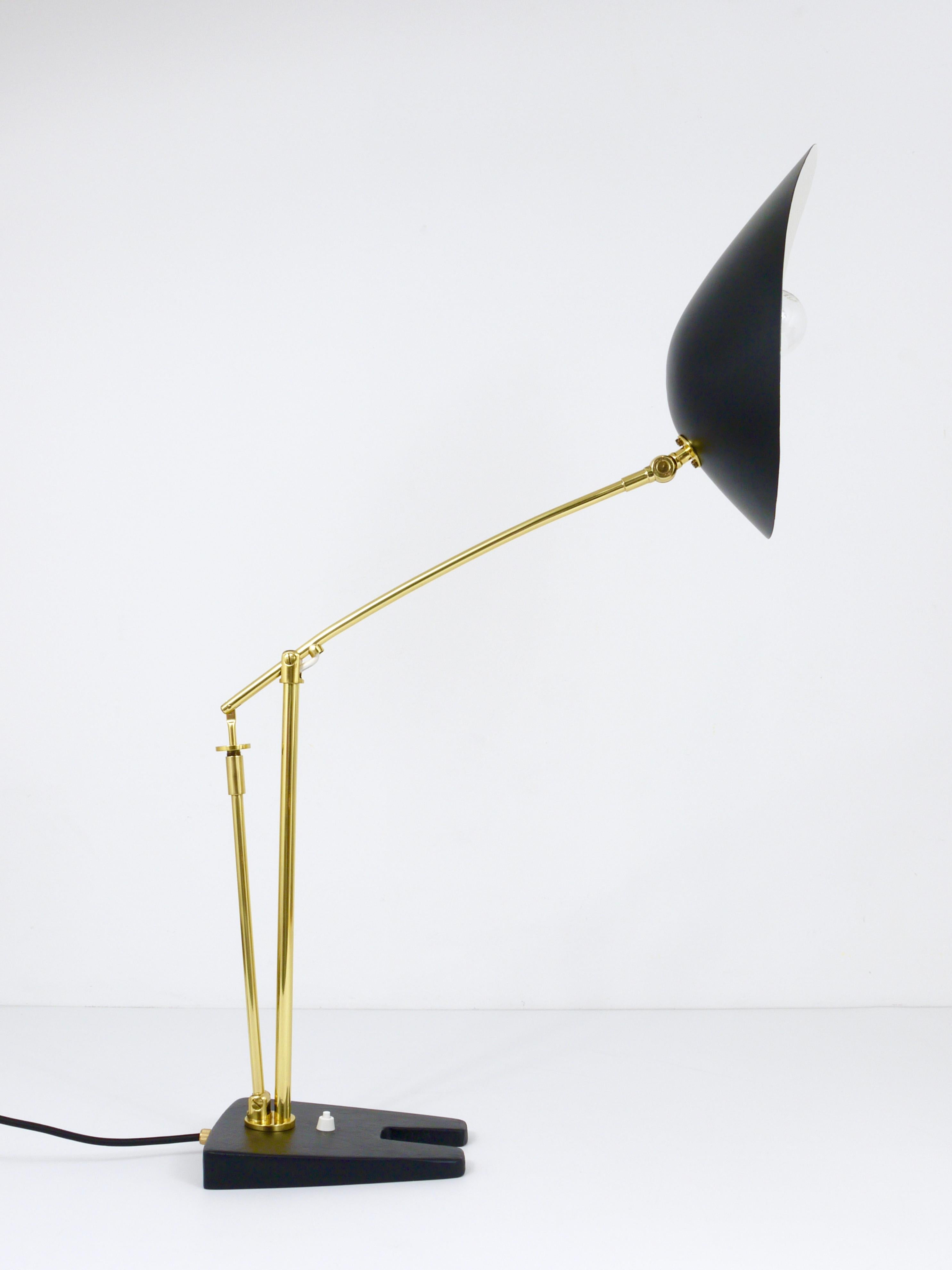 A French articulating height adjustable brass table or desk lamp from the 1950s. This iconic light is made of brass and has an amazing adjusting system, a pivotable black lacquered aluminum lampshade and a solid cast iron base. The lamp has been