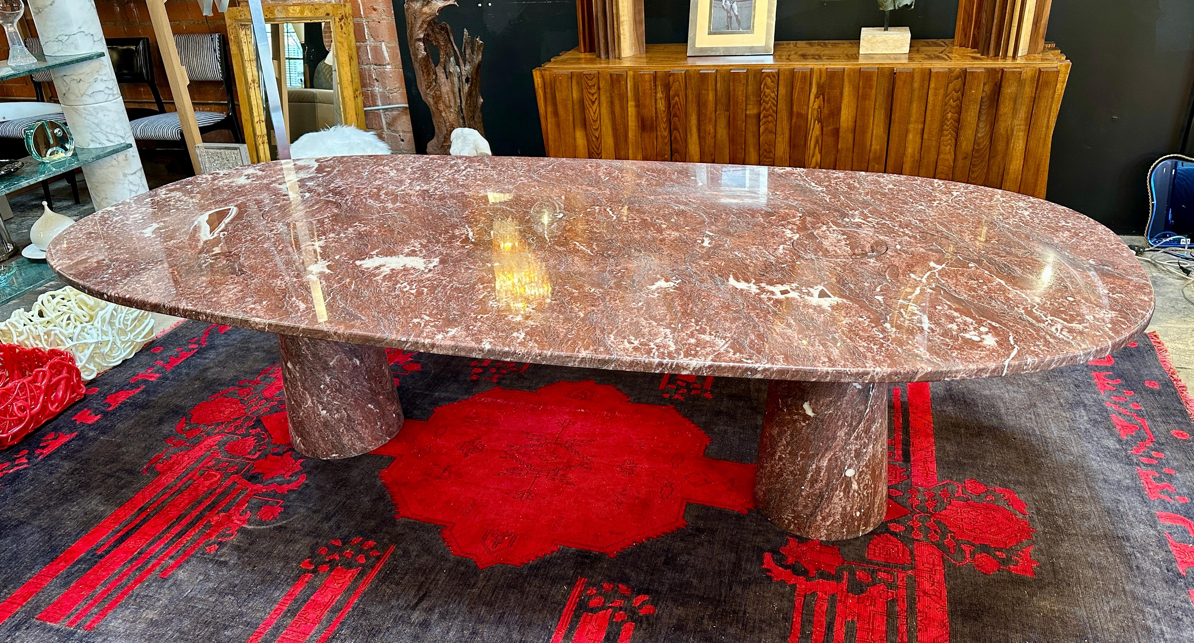 Questo tavolo da pranzo in marmo di Angelo Mangiarotti, dalla forma ovale, presenta un piano in marmo rosso-marrone con venature bianche naturali che aggiungono eleganza e interesse visivo. Il tavolo poggia su due basi cilindriche in marmo, che gli