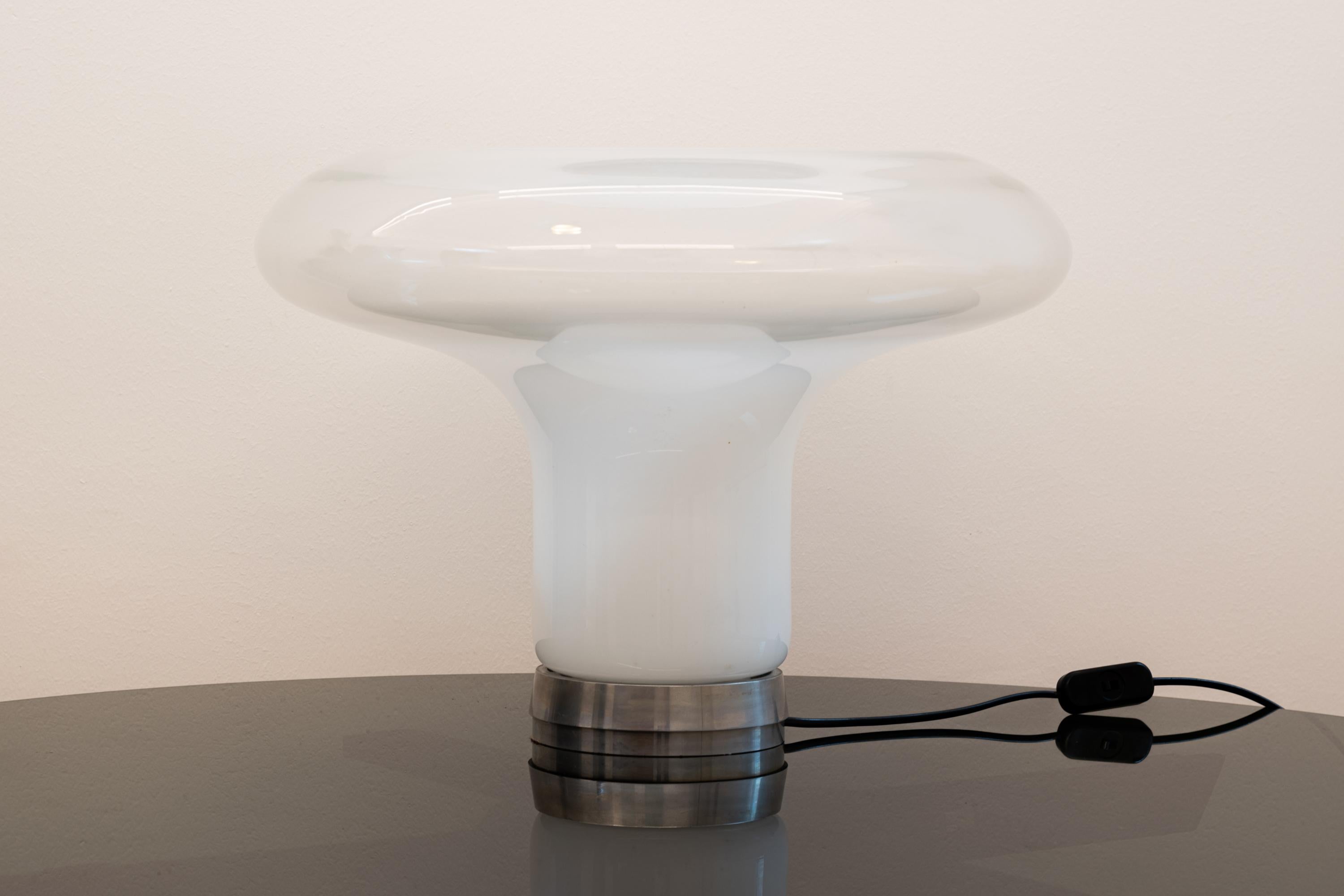 Lesbo table lamp with a polished metal base with a diffuser made of a single hand blown Murano glass element.
The beautiful shape of the diffuser and the peculiar white-transparent shades of the glass is obtained thanks to the excellent know-how of