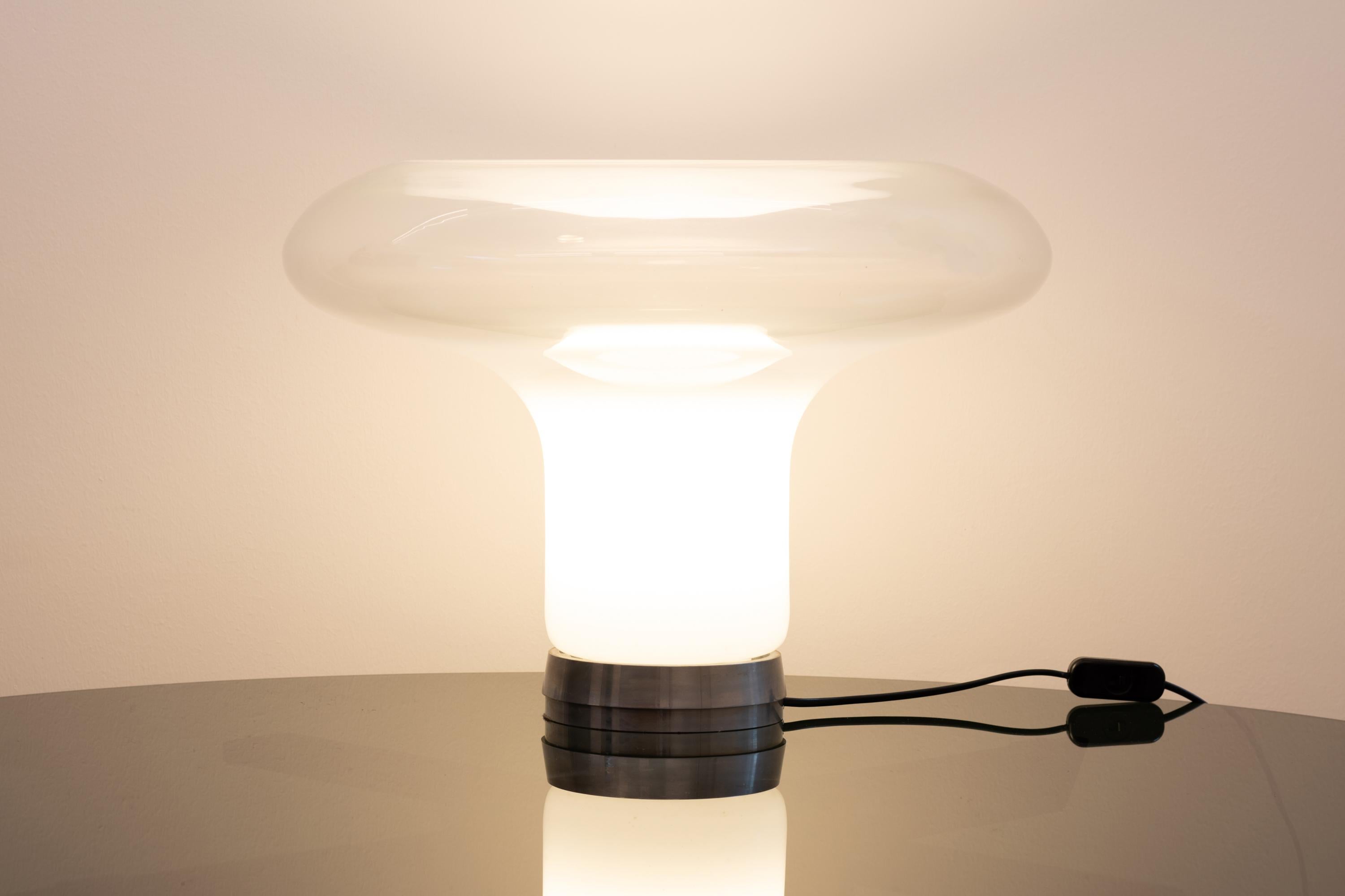 Lampe de table Lesbo avec une base en métal poli avec un diffuseur composé d'un seul élément en verre de Murano soufflé à la main.
La belle forme du diffuseur et les teintes blanches-transparentes particulières du verre sont obtenues grâce à