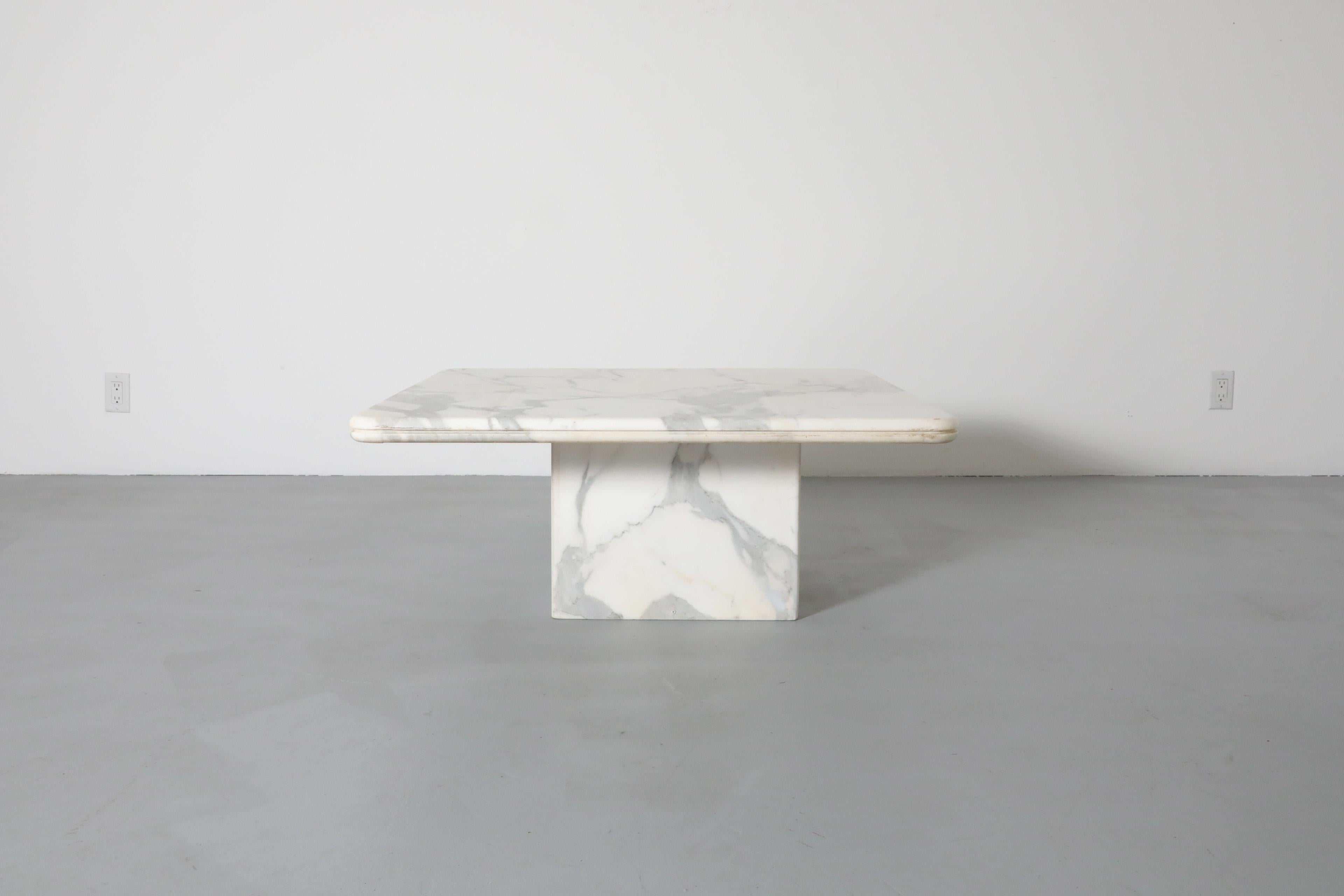 Elegante tavolino in marmo modernista. Il pesante piano di marmo quadrato con angoli curvi e bordi scanalati poggia su una base di marmo a forma di cubo. In condizioni originali con alcune irregolarità evidenti, tra cui graffi, scheggiature, segni
