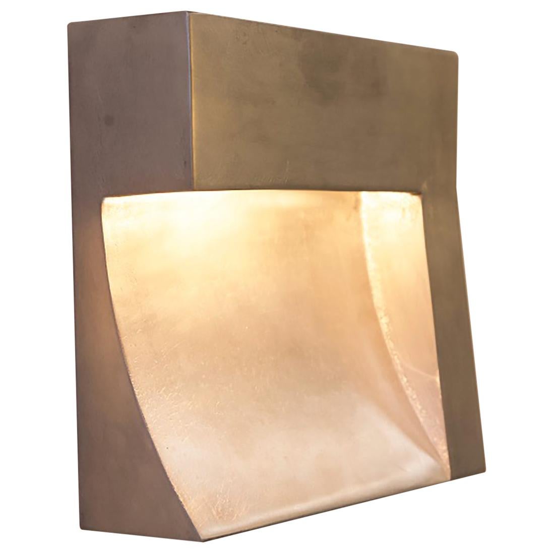 The Angle is a sculptural wall light in cast aluminum. A sweeping arc of light is carved into the face of the fixture bringing balance to its Brutalist form. The casting is finished to a smooth texture and is available in silver, bronze or matte