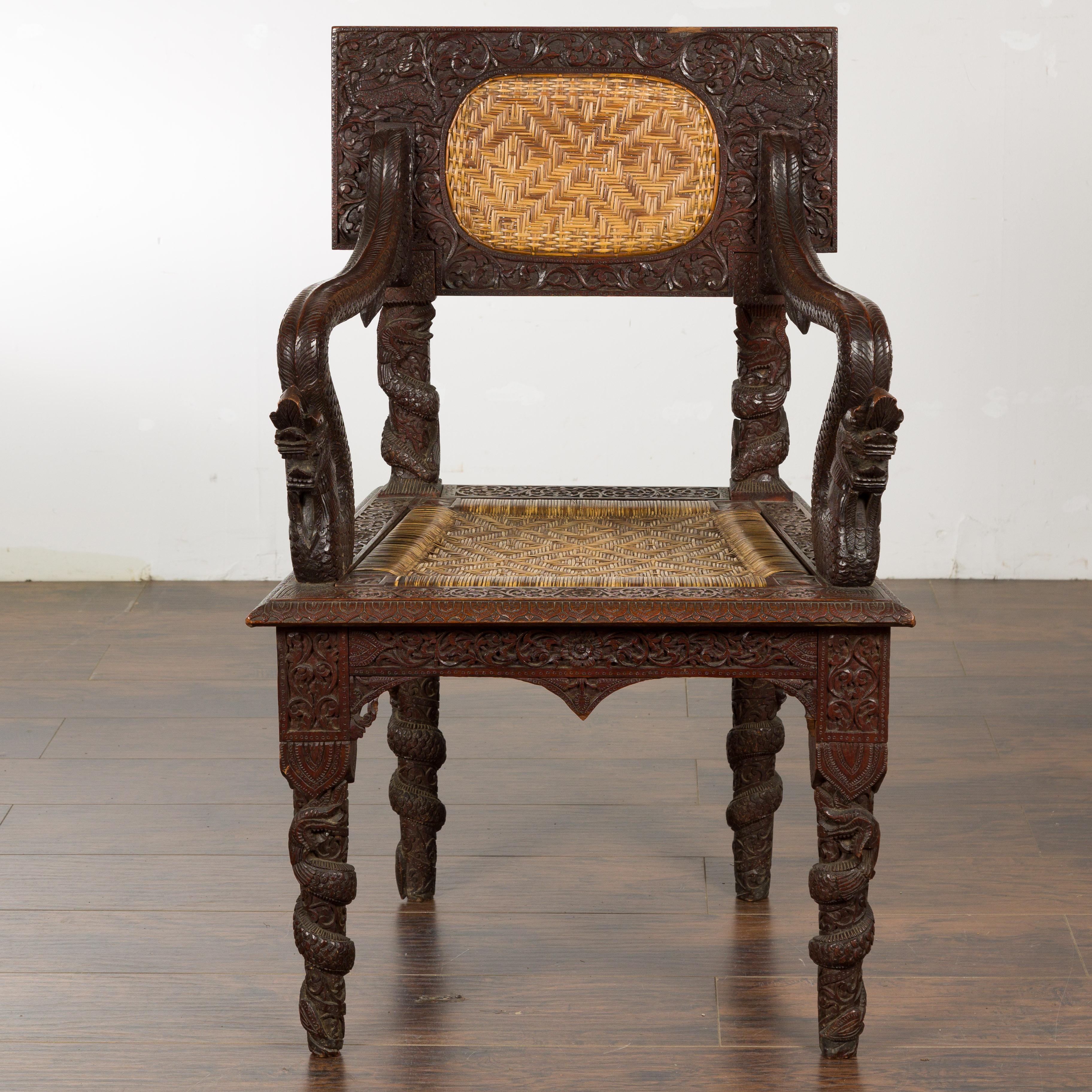 An Anglo-Indian carved wooden armchair from circa 1900 with carved back and mythical creatures on the arms. This magnificent Anglo-Indian carved wooden armchair, dating from circa 1900, is a striking blend of intricate craftsmanship and storytelling