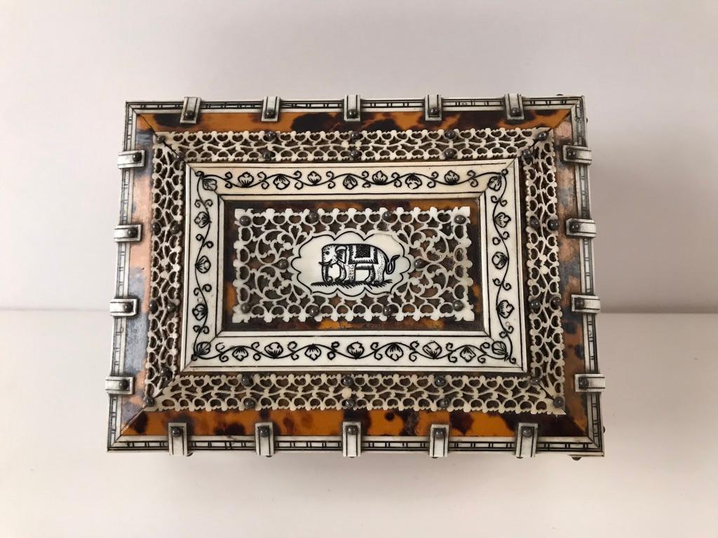 19th century Anglo-Indian desk-top box made of sandalwood veneered with tortoiseshell overlaid with intricate pierced bone panels and banding on four lion's paw feet. The central panel on top decorated with a incised drawing of an elephant in black