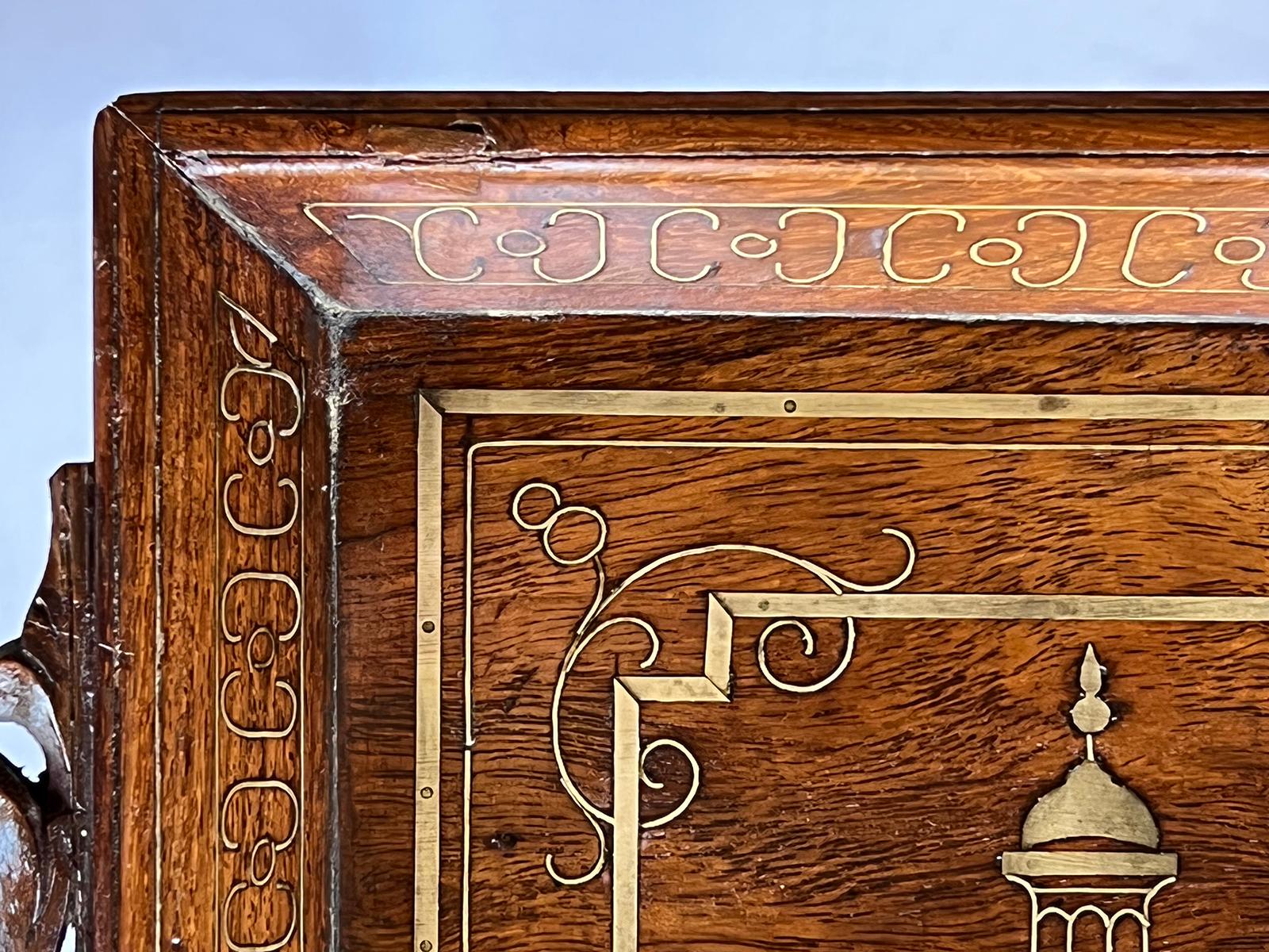 With turned fold-down legs, the rectangular tray centering a brass inlaid Taj Mahal (commissioned in 1631 by the Mughal emperor Hhah Jahan to house the tomb of his wife, Mumtaz Mahal); the canted sides of the tray dovetail joined and decorated with