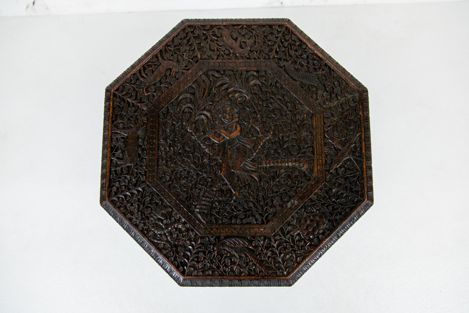 Anglo-Indian carved octagonal teak wood table, top is carved with a flute player in the central cartouche. It is bordered with stylized deer, dogs, birds, pine cones, and salamanders.
 