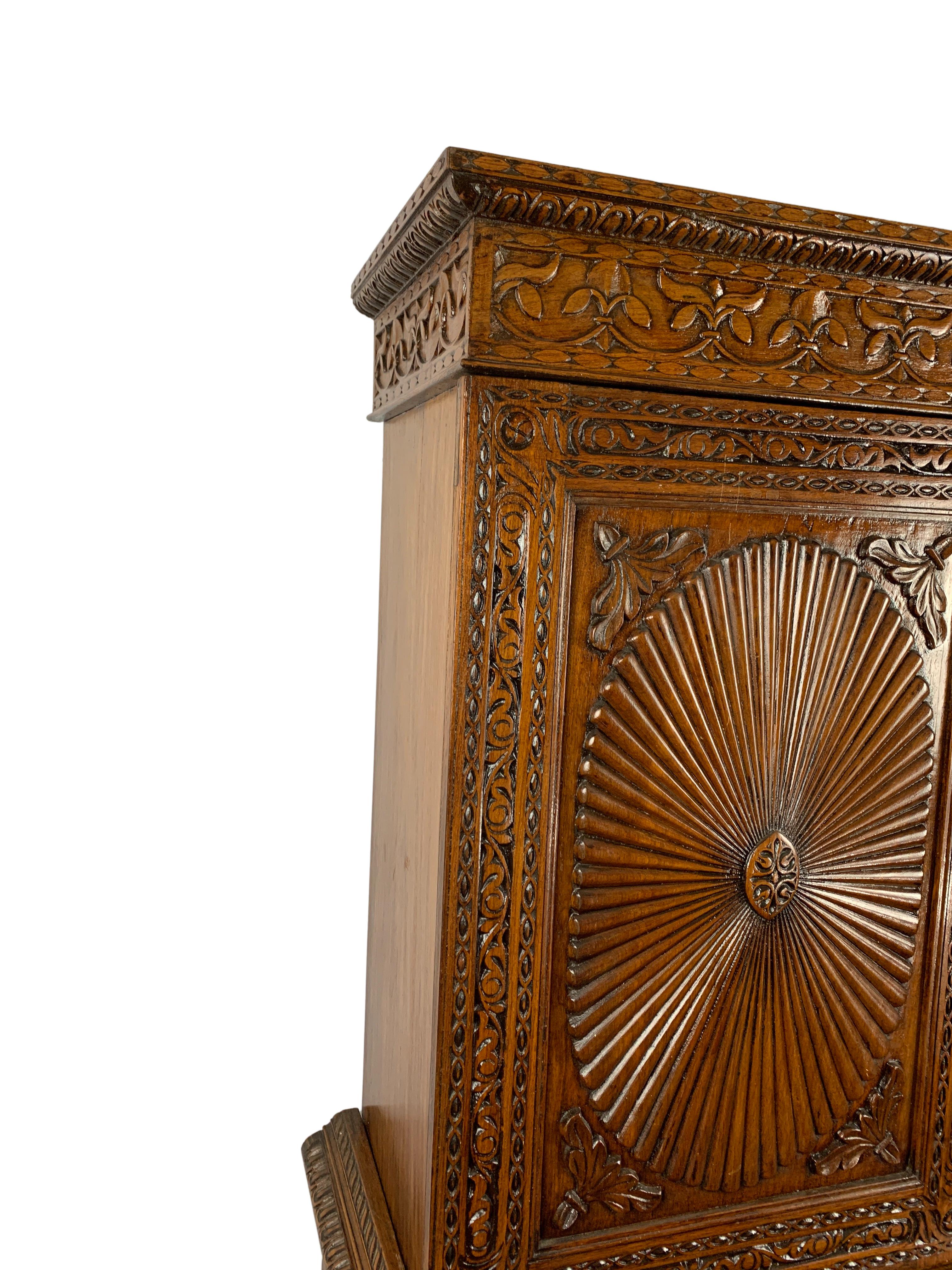 Anglo-Indian linen press with four carved sunburst paneled doors, floral carving through out and raised on bun feet. The upper and lower case each with two shelves, 19th century probably made in Bombay.
 