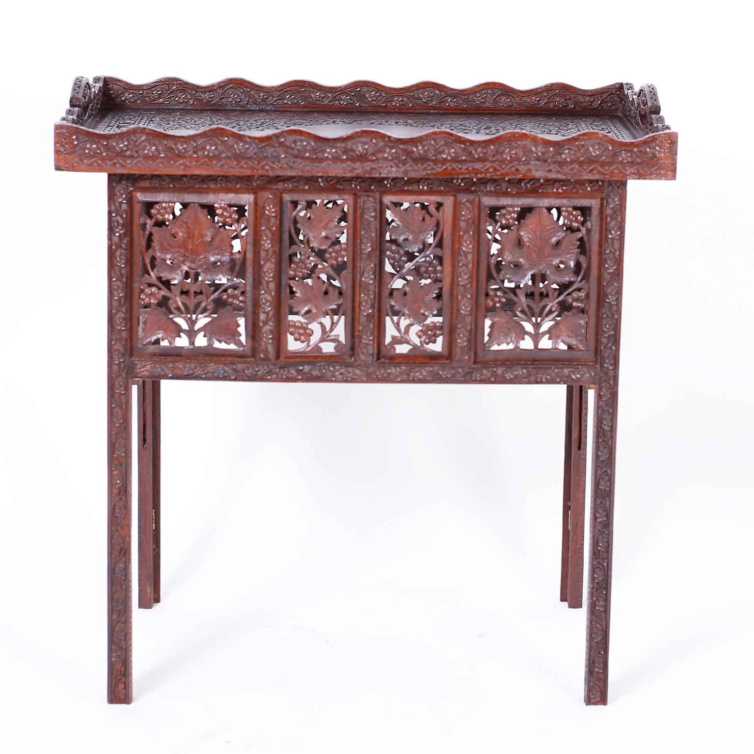Anglo Indian table crafted in mahogany with a removable serving tray ambitiously carved with floral designs and a base with carved leafy panels of open fretwork on elegant carved legs.