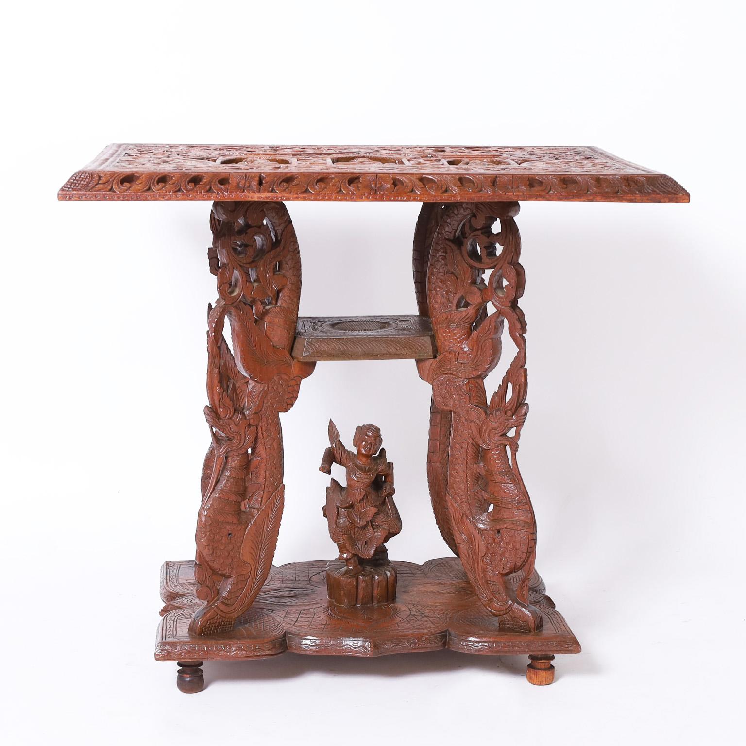 Antique Anglo Indian stand with a dramatic form, crafted in mahogany with an elaborately carved rectangular top depicting niches, gods, and deities in a floral field, supported by four carved dragon legs on a platform with a dancing figure.