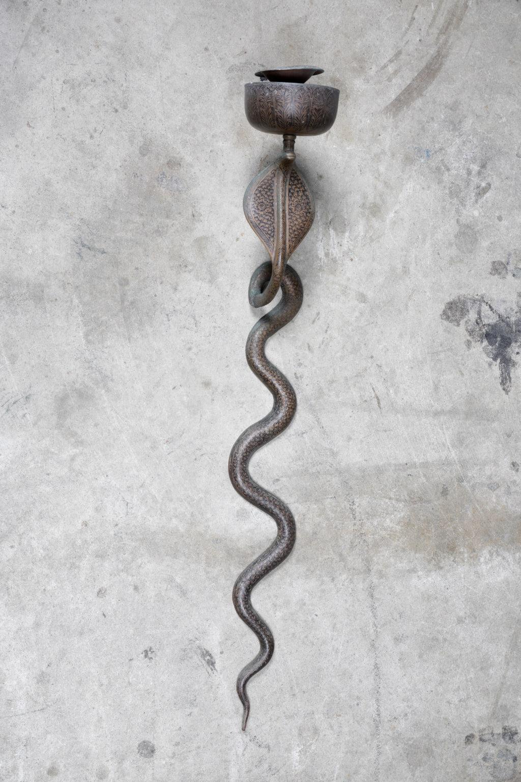 A single early 20th century Anglo-Indian cast brass wall sconce in the form of a snake or cobra. The sconce holds a tapered candle and has black enamel details all-over.