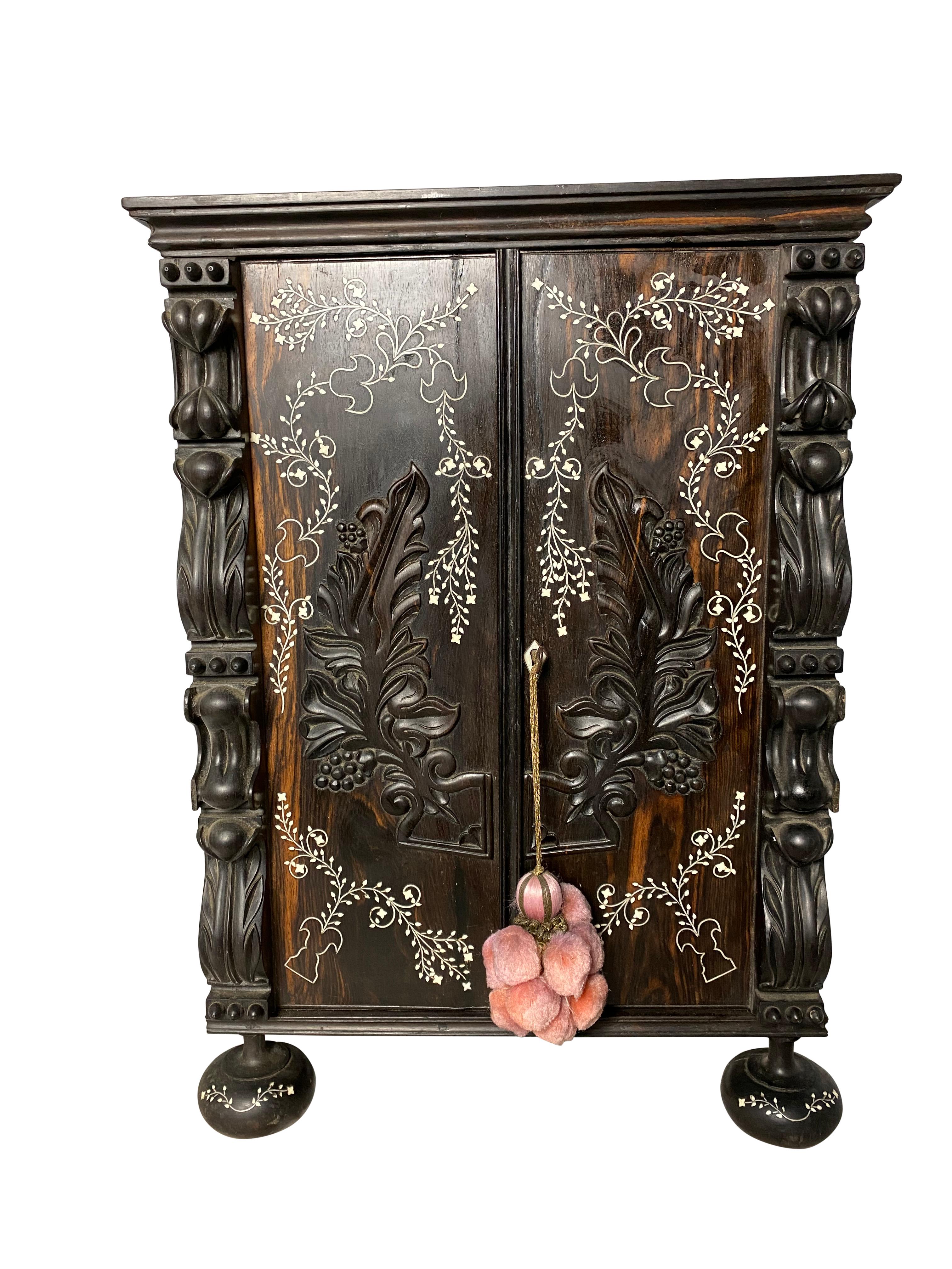 A dark Anglo-Indian ebony inlaid cabinet from the 19th century. With large spaces inside for storage and with both floral carvings and embellishments, this cabinet is suitable for both decoration and use. 

Dimensions (cm)
H50/W34/D22.