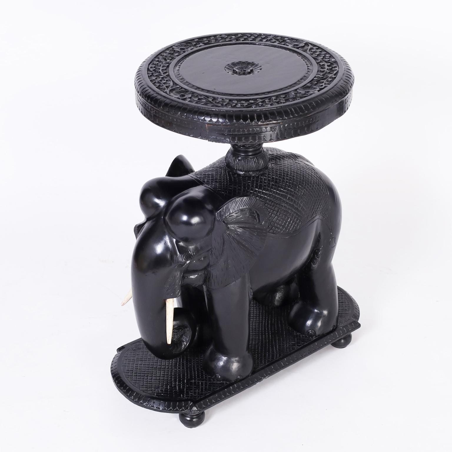Anglo Indian stand or table crafted in indigenous hardwood having an ebonized finish with a round top carved with floral designs on a carved elephant base with bone tusks on a platform with turned feet.