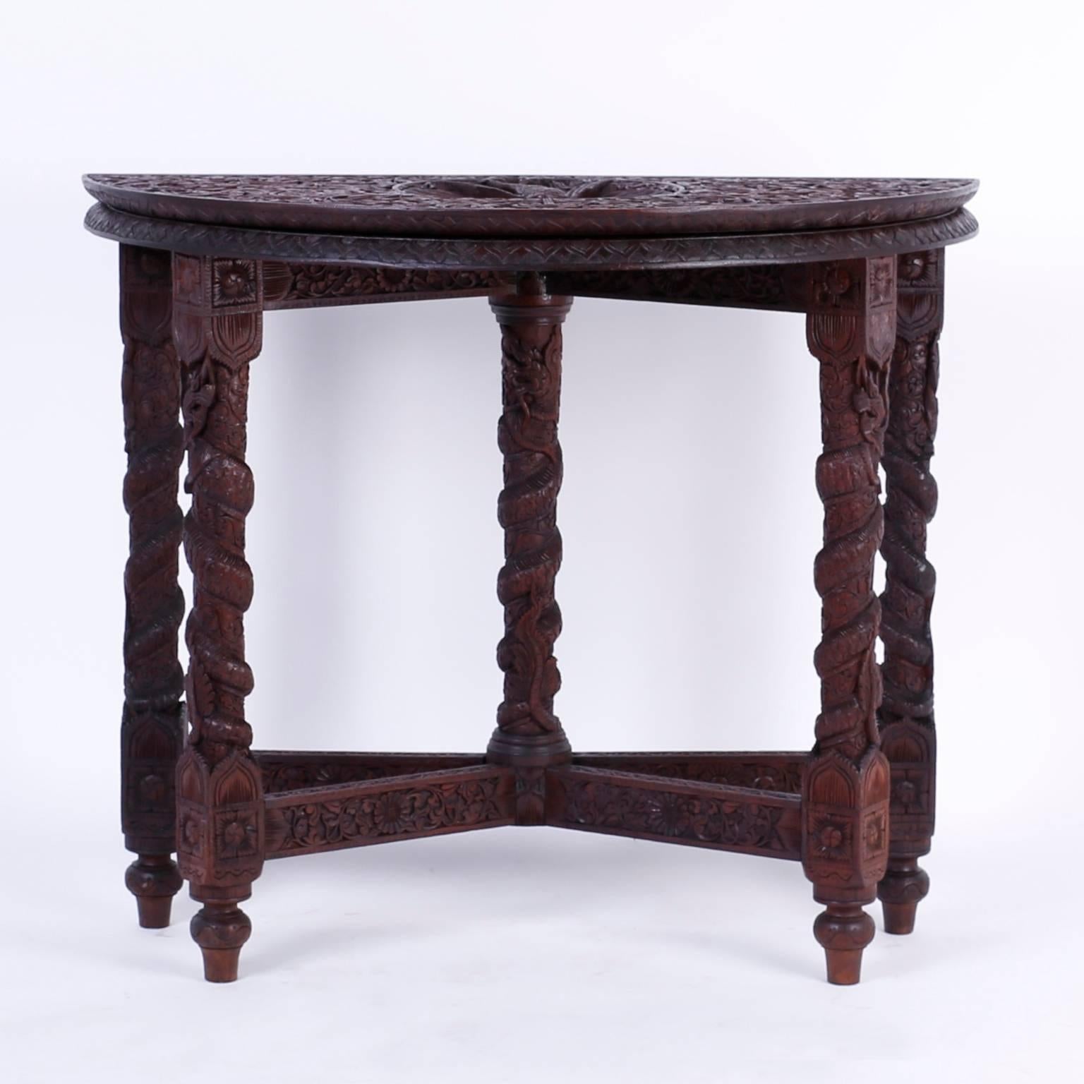 Inspired mahogany Anglo-Indian game table that when folded is a demilune console with an elaborately carved top featuring a centre peacock in a floral field. When opened to a round game table it reveals four panels of carved animals and an open