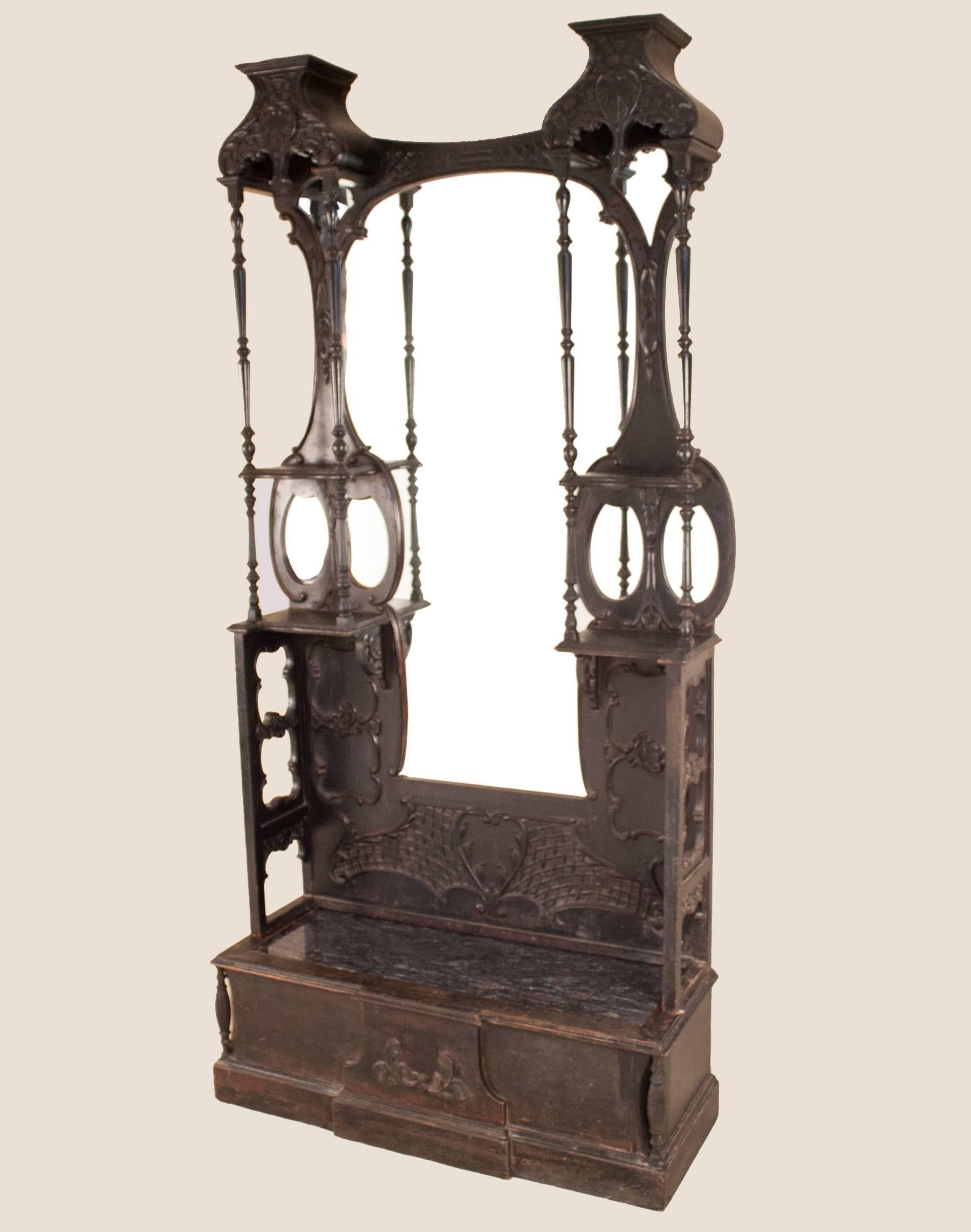 An ebonized mahogany hall mirror and bench from eastern India with a hand-carved frame and decorative details, original full-length mirror and side mirrors, four display shelves, and a bench with recessed granite slab. This grand hall Stand is