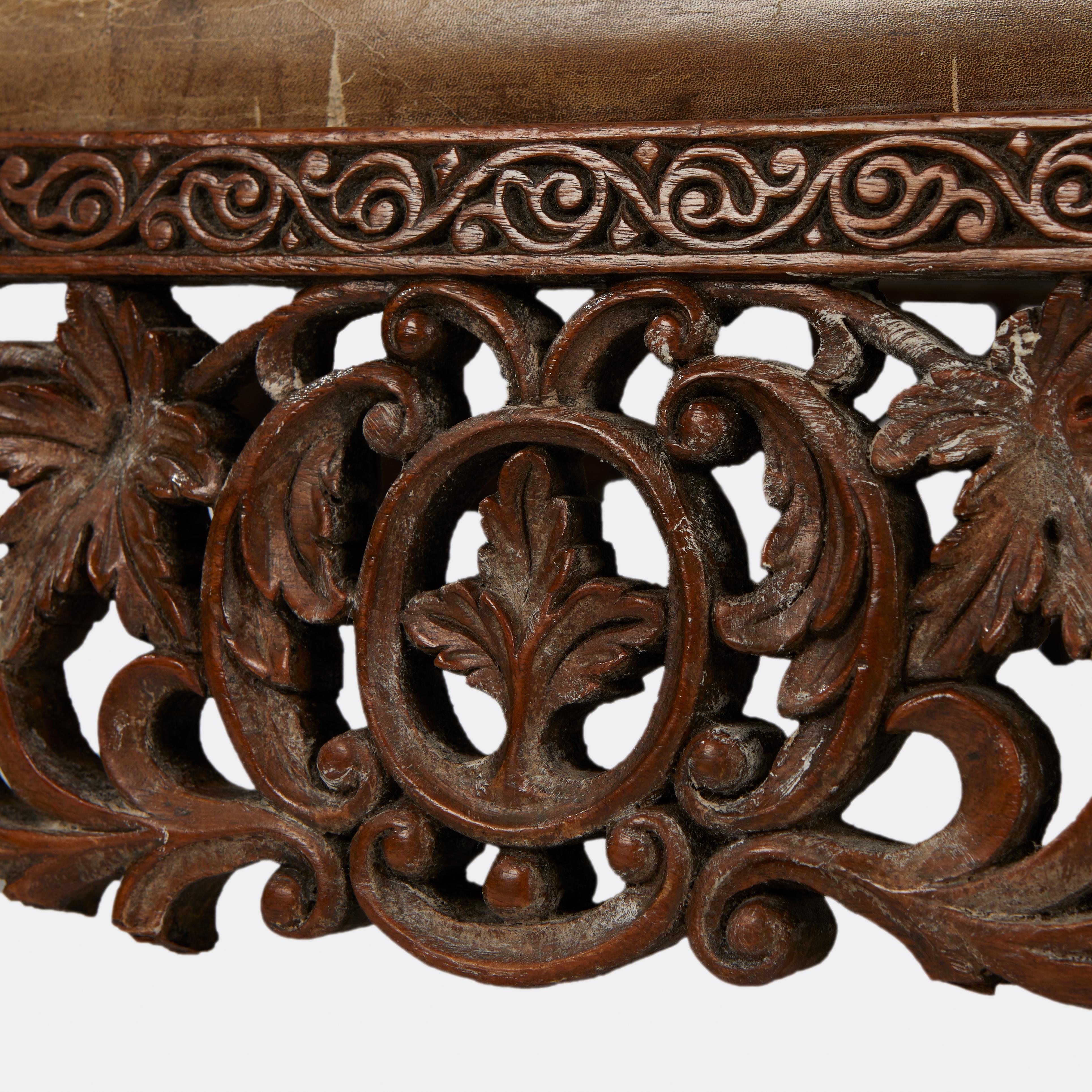 An Anglo Indian hand-carved padouk wood low bench with hand-carved cabriole legs with carved apron wood. Seat upholstered in distressed leather. Circa 1880s.
 