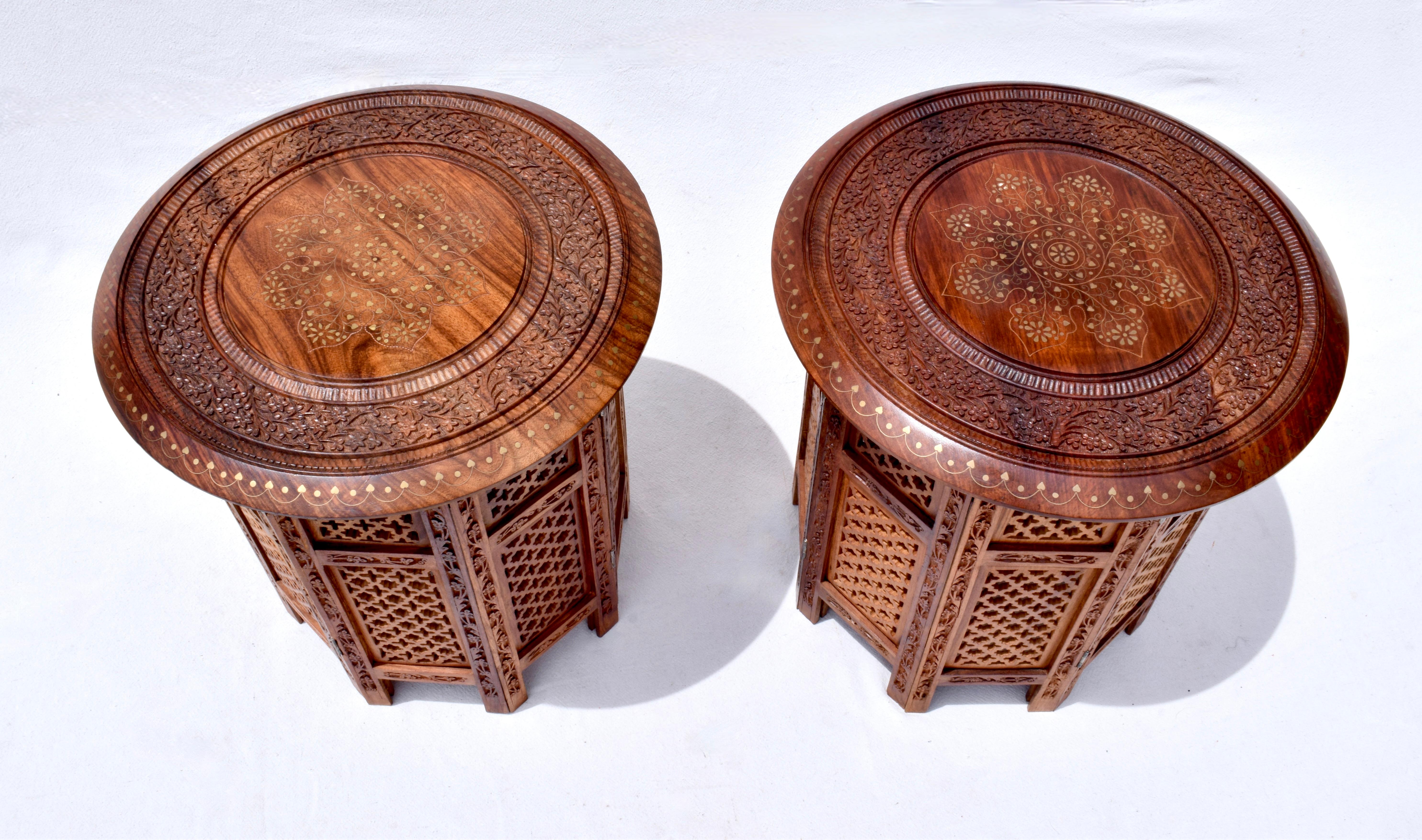 A versatile, standout pair of 1950's Anglo Indian stands, stools or tables, hand crafted in teak wood having round tops with intricate brass inlays and floral carvings. Tops detach on collapsible pierced bases, the overall aesthetic giving the