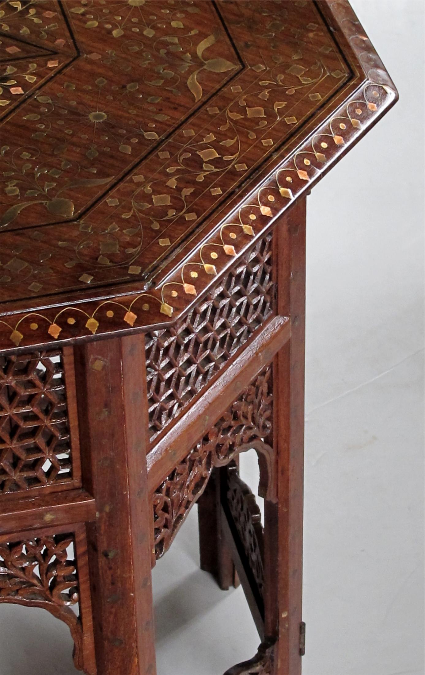 Originally used as traveling tea tables for the British in India; the octagonal top with central star medallion surrounded multiple geometric and foliate designs within an outer foliate vine border; raised on a hinged base with open fretwork;