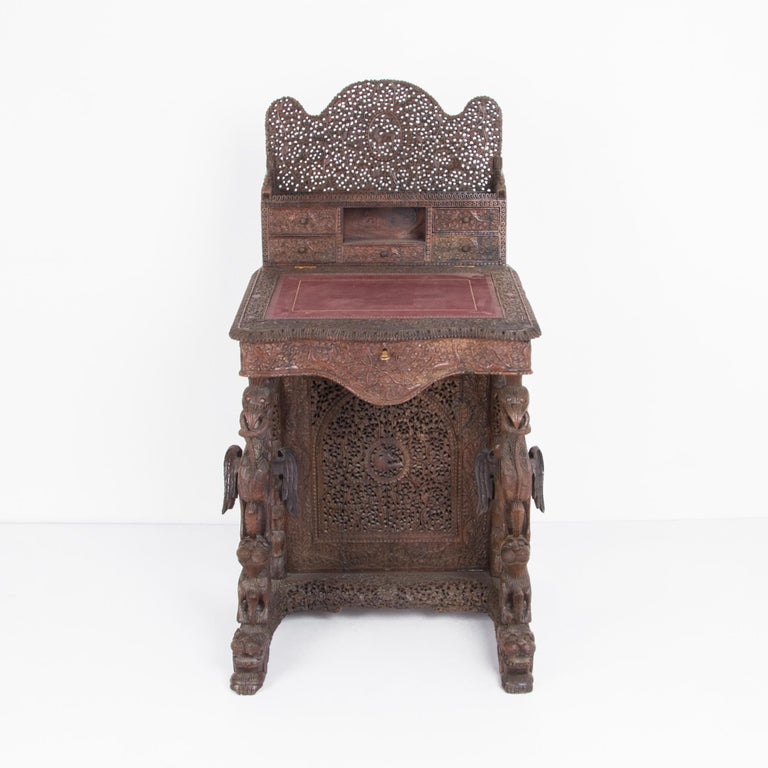 A carved writing desk from the United Kingdom, circa 1900. This rare colonial inspired piece is carved from tropical hardwood in ornate detail. Tropical birds and crouching lions support a handy writing surface. Pigeon-hole drawers and interior