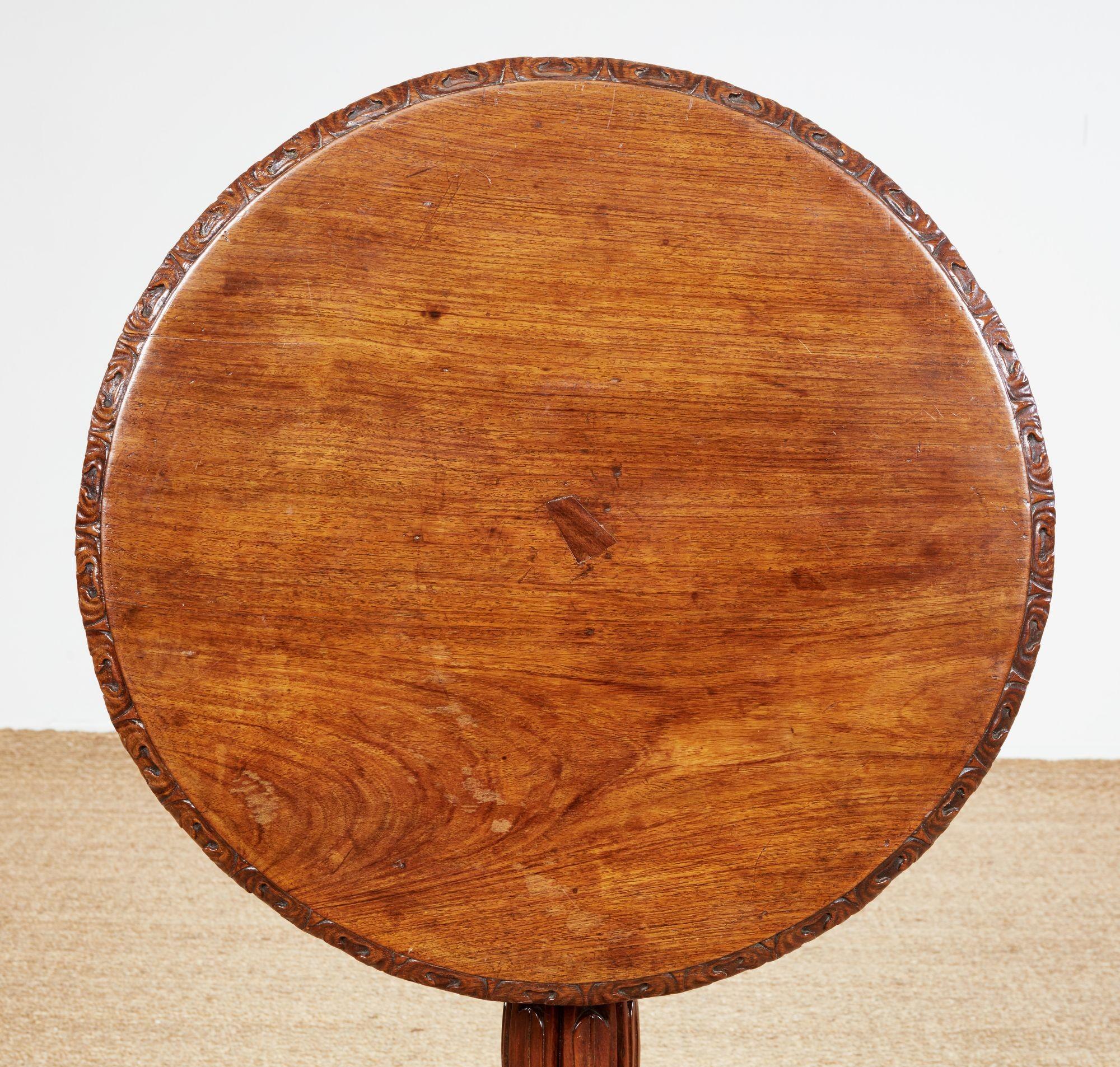 Mesa de acento de madera de padouk tallada a mano, de finales de la Regencia, con tablero circular inclinado y delantal tallado con motivos foliados, sobre un pie torneado muy elaborado y una base trípode cóncava que termina en patas torneadas.