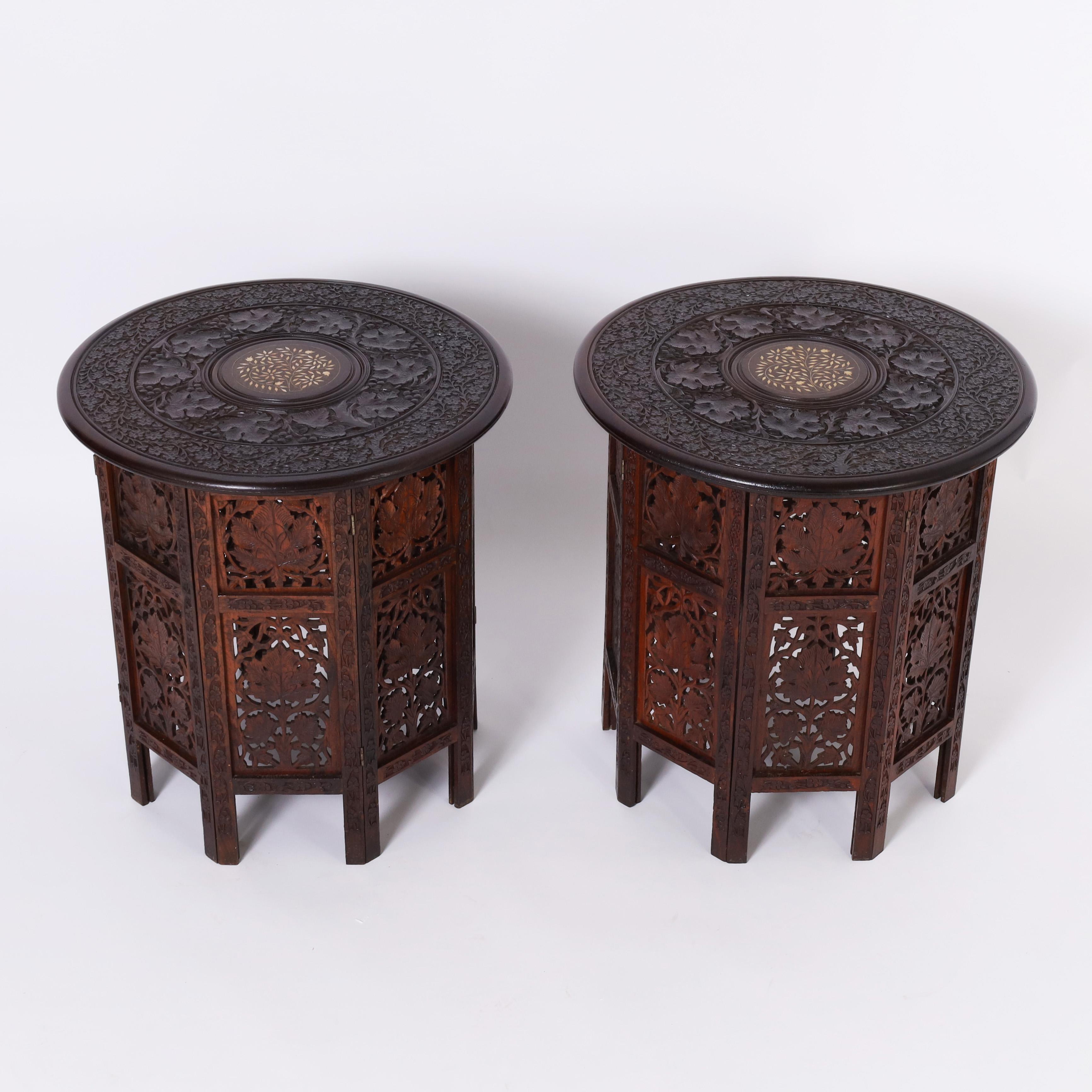 Impressive pair of British colonial stands handcrafted in mahogany having round tops elaborately carved with floral motifs and a center medallion with inlaid bone flowers. The octagon bases are floral carved with open fretwork. 
