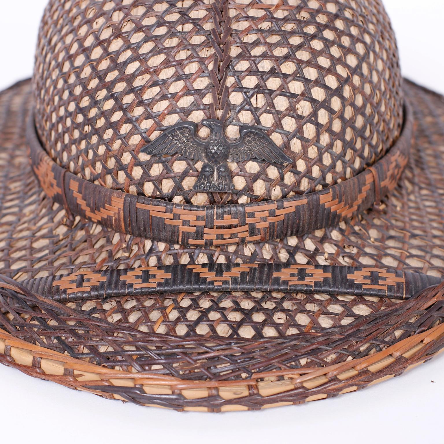 Rare and unusual vintage Anglo-Indian pith helmet with decorative appeal crafted in rattan and wicker with woven geometric symbols and a carved wood eagle on the front. 



 
