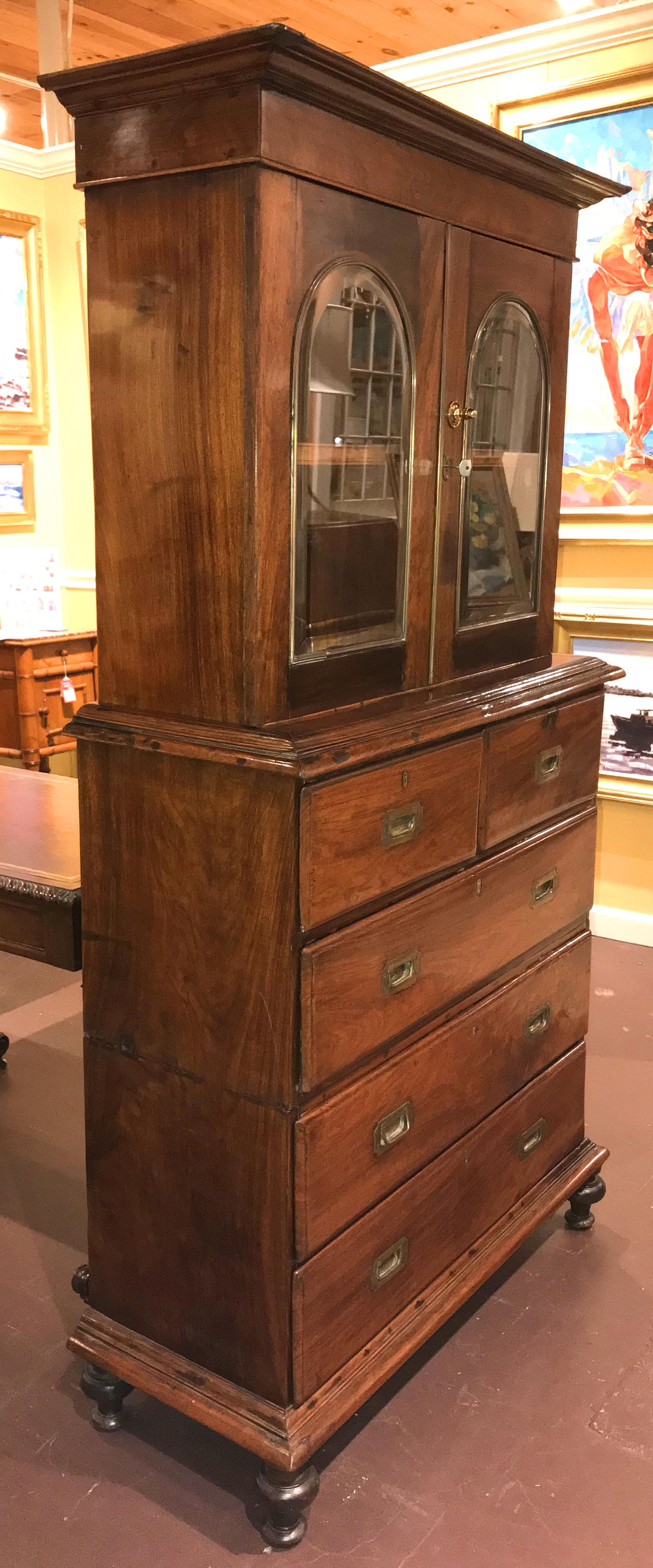 A unique form three-piece Anglo-Indian rosewood Campaign chest, possibly a sea captain’s chest or cabinet, featuring a bookcase top with molded cornice, surmounting two doors, each with brass trimmed arched beveled glass, which open to a single