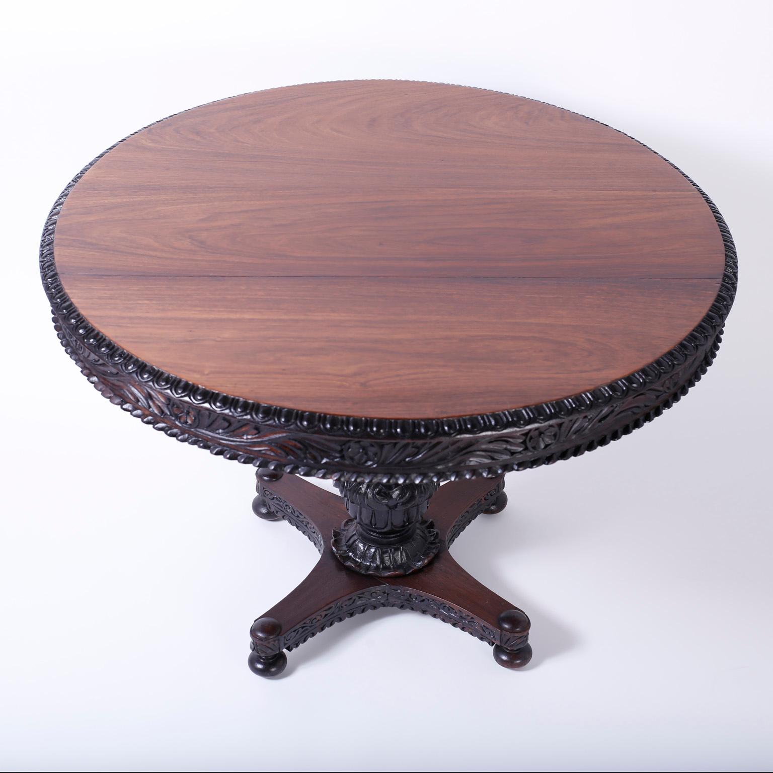 Refined Anglo-Indian round tilt-top dining or centre table crafted in rosewood with a dramatic wood grained top, floral carved skirt, carved acanthus leaf pedestal and a four legged base on bun feet.